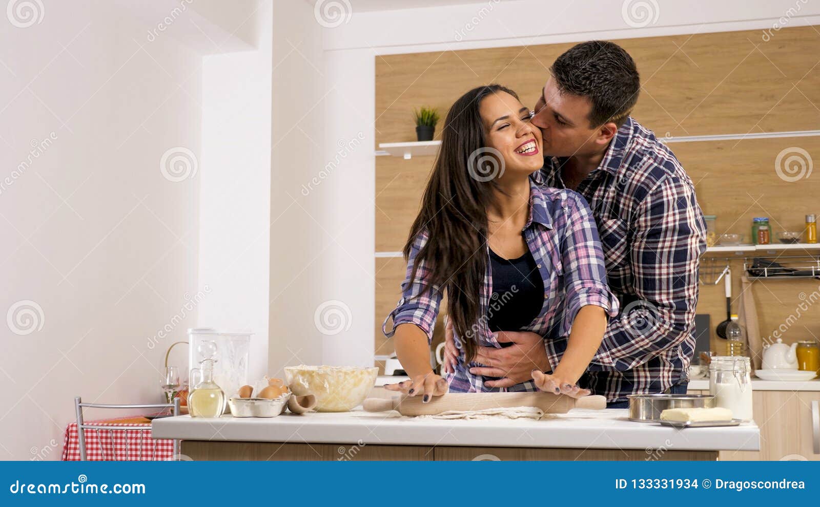 young wife giving affection to her husband while cooking