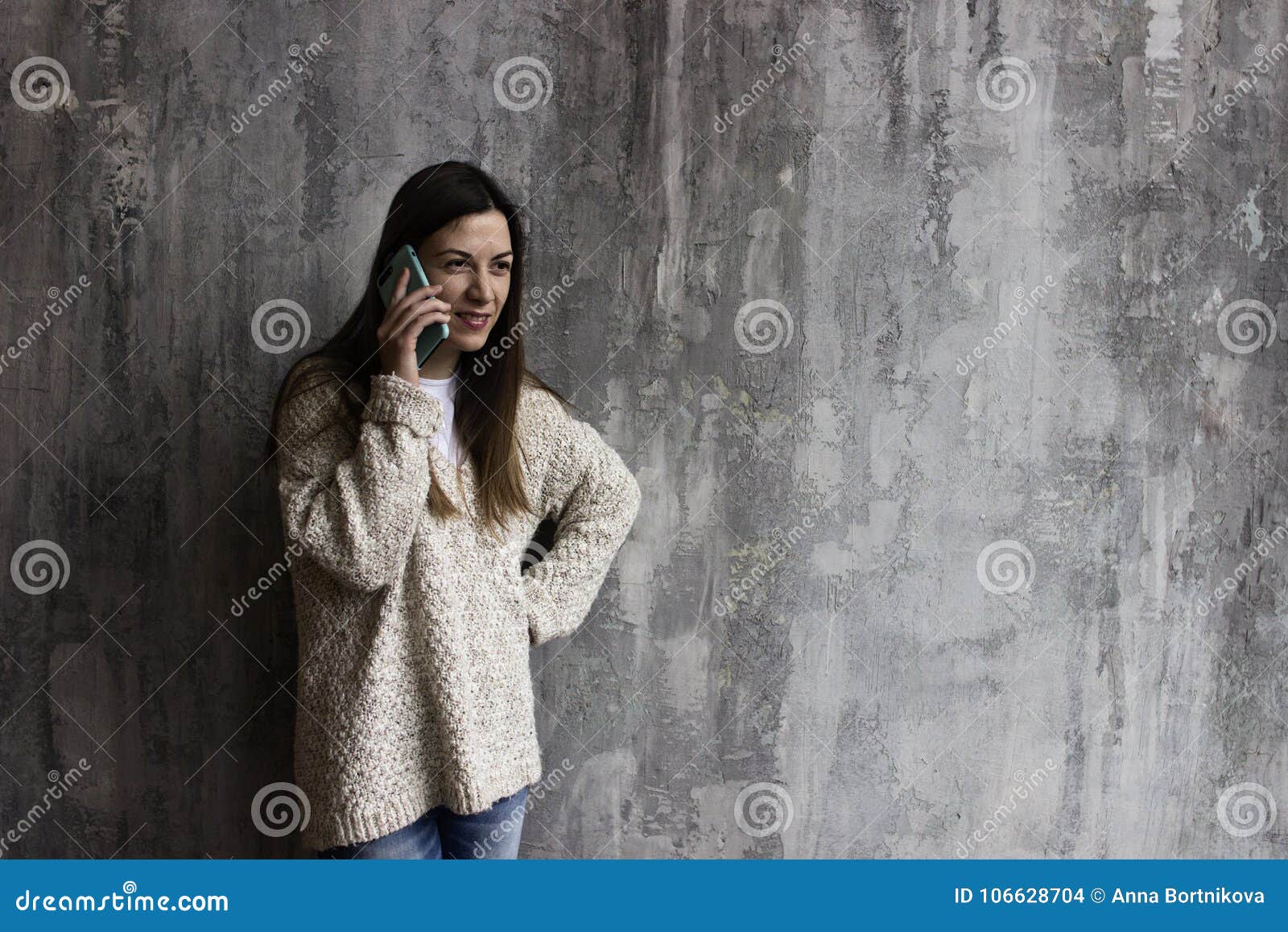 Young Woman in a Beige Cardigan Stands Against the Gray Wall and Stock ...