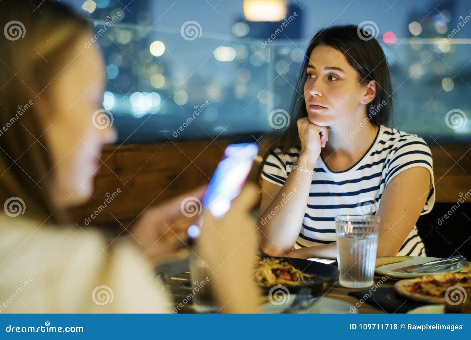 young woman being bothered by a friend using a smartphone smartphone addiction and social issue concept
