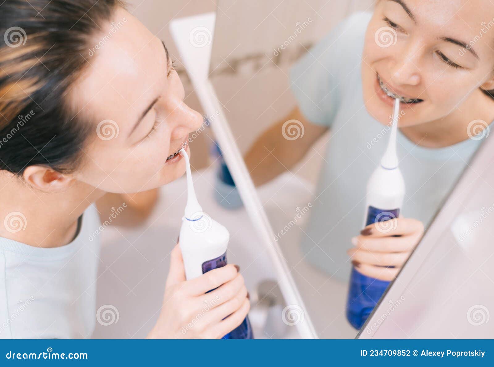 woman with braces on her teeth brushing her teeth with by using a irrigate, before mirror, top view.