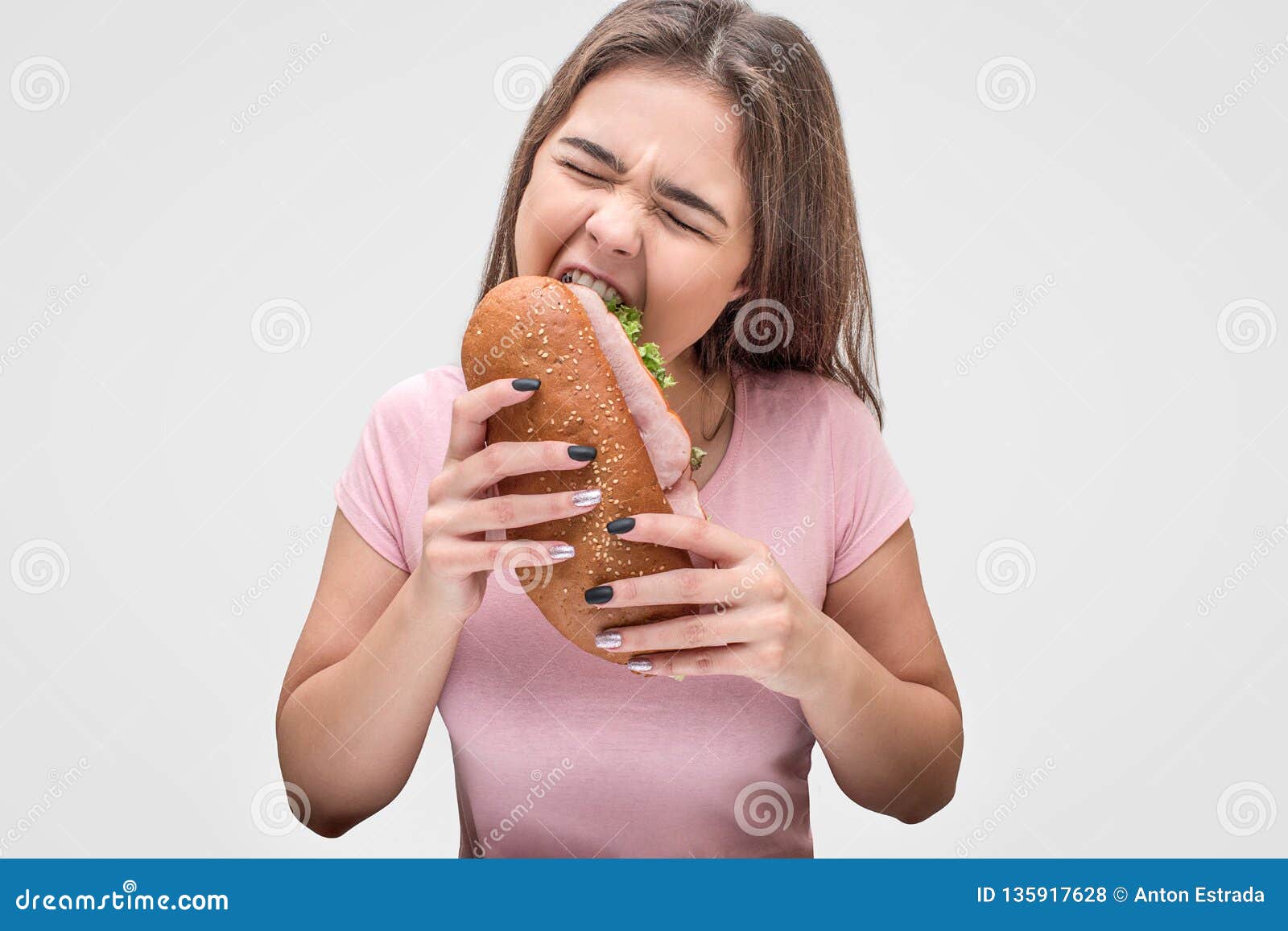 young woman devour sandwich. she hold it in hands and keep eyes closed.  on grey background.