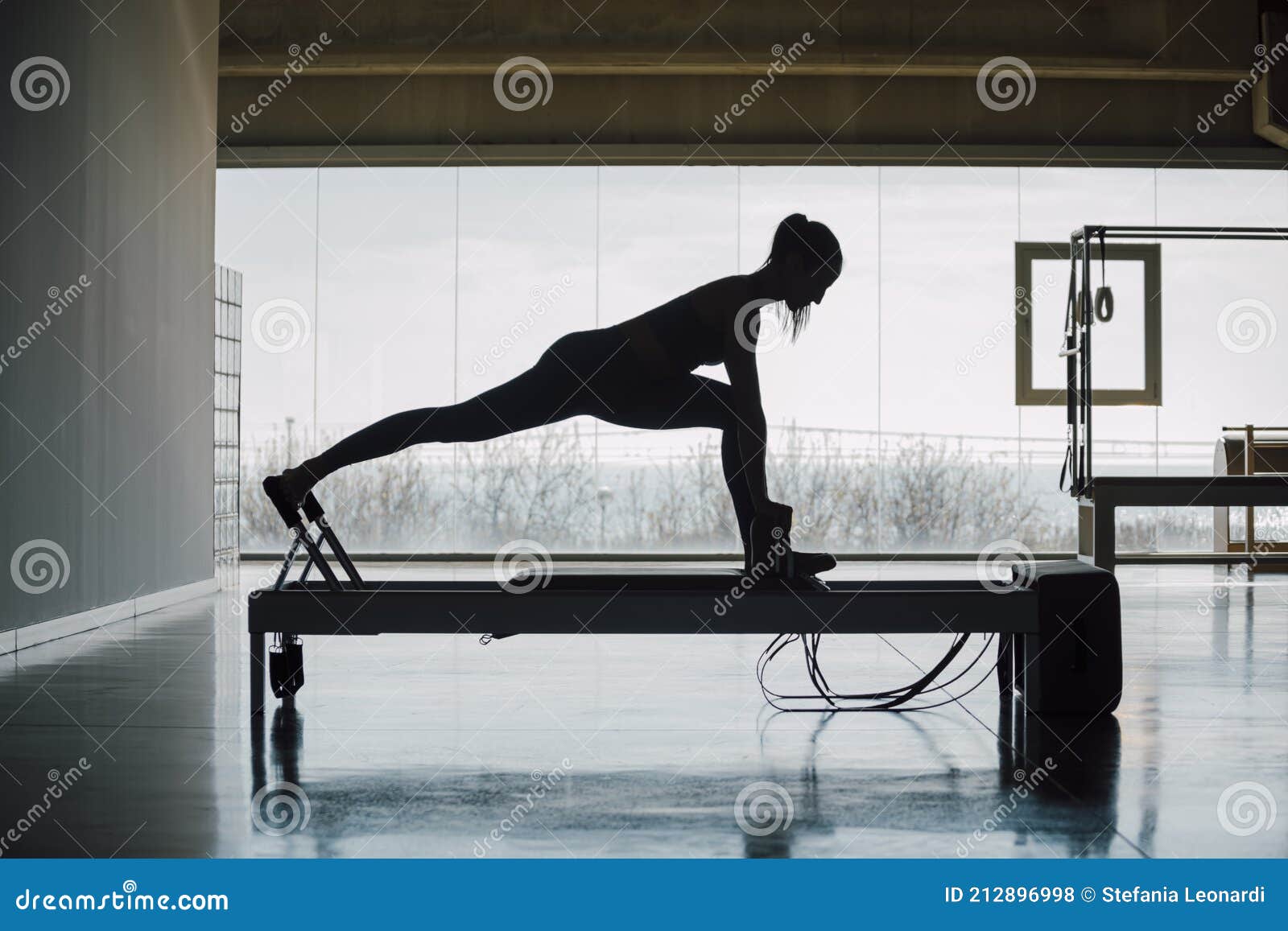 flexible female using pilates reformer machine in gym