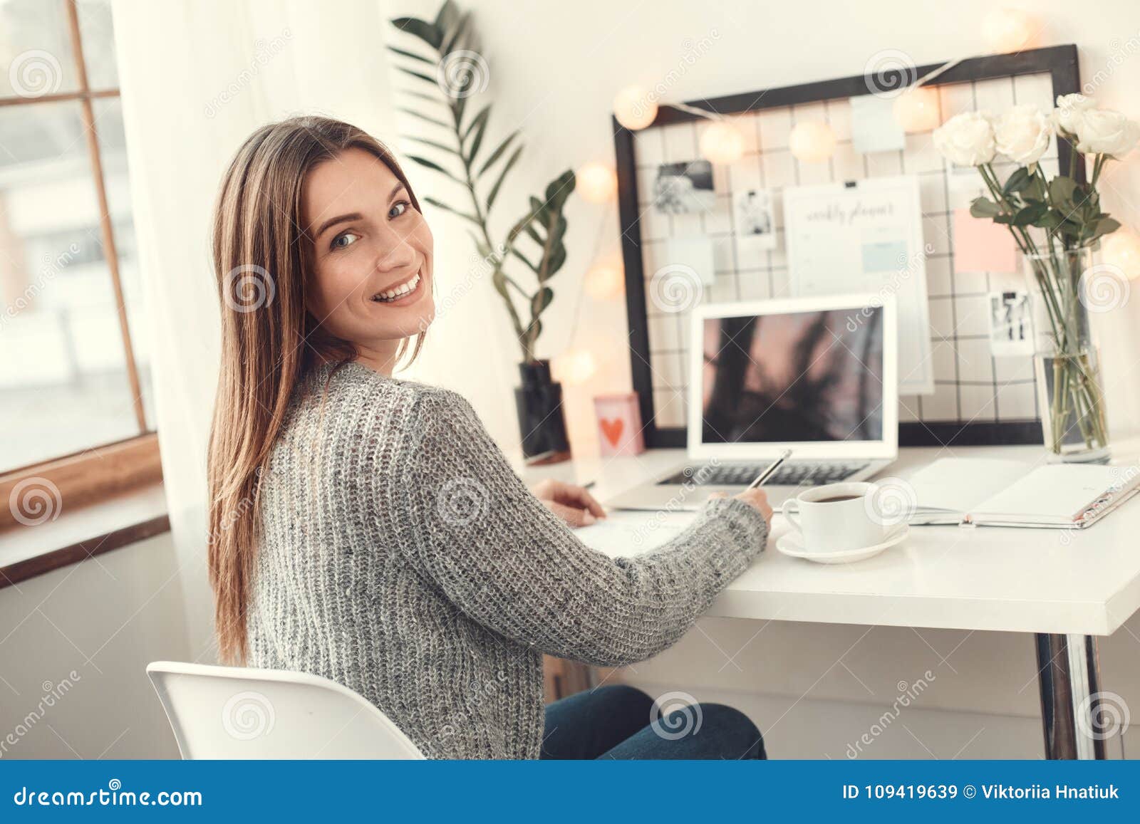 young woman freelancer indoors home office concept winter atmosphere sitting writing in planner smiling