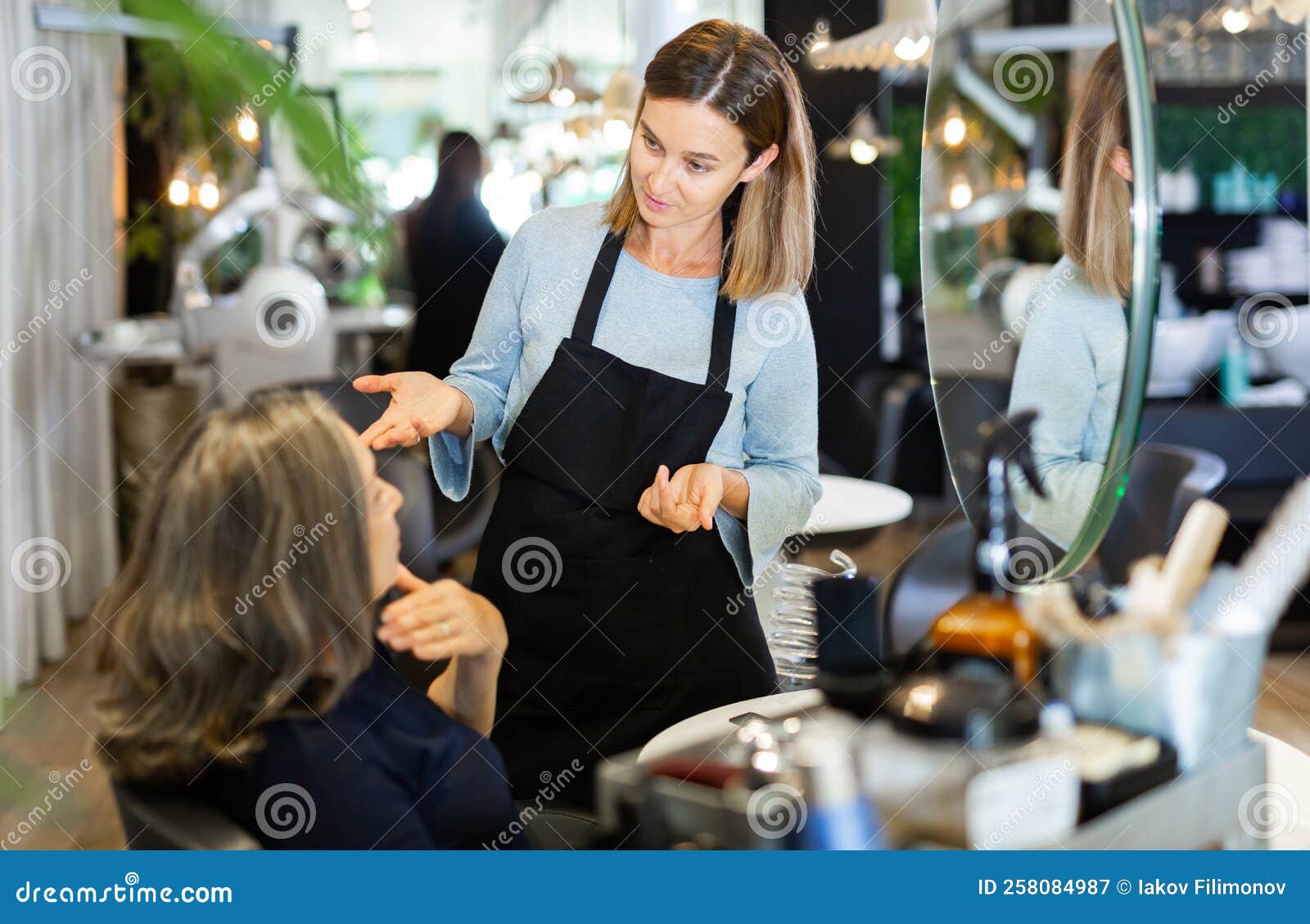 Young Woman Hair Stylist Talking To Elderly Female Client in Salon ...