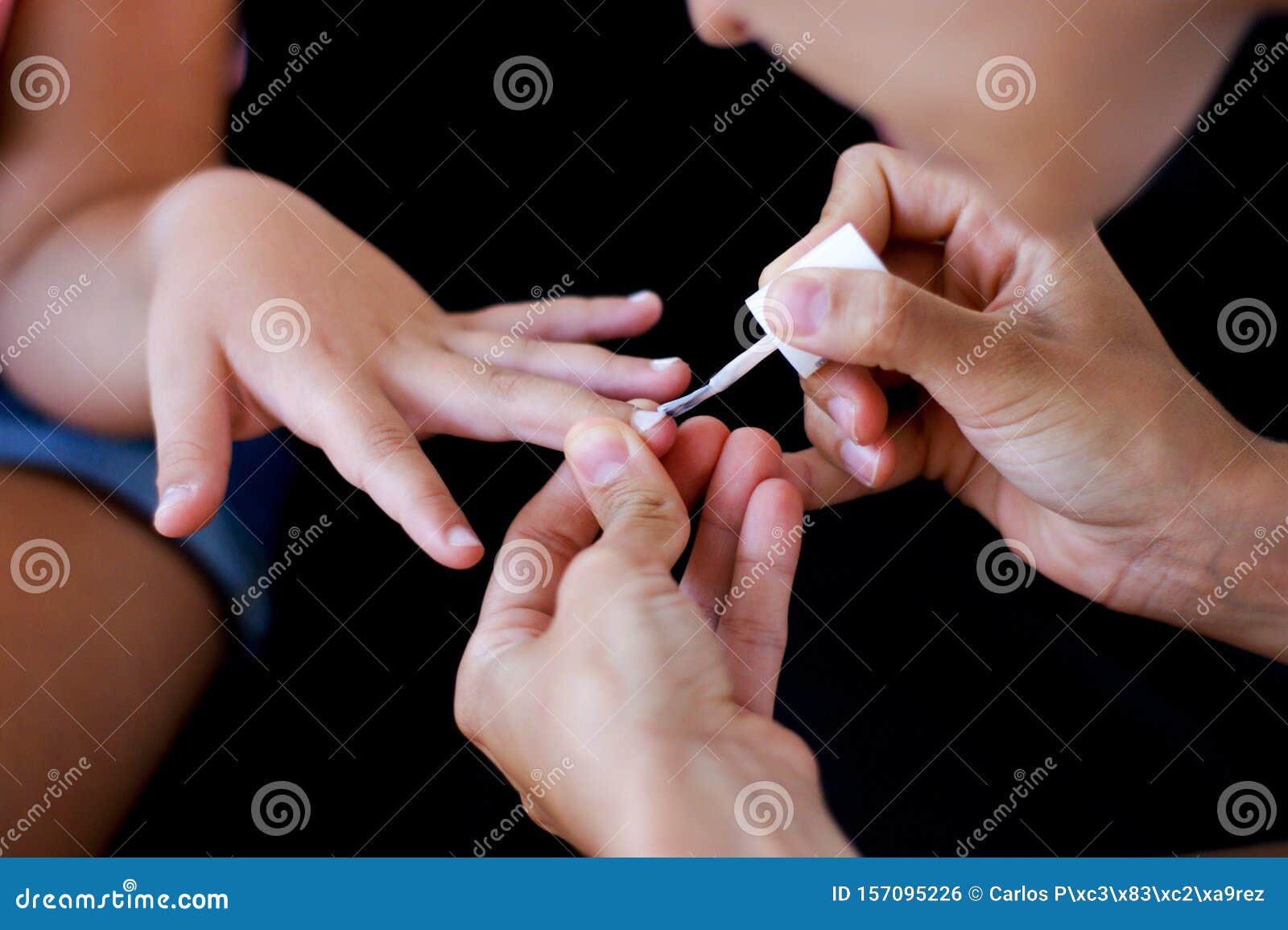 young woman hands painting little girl nails with whitish gloss