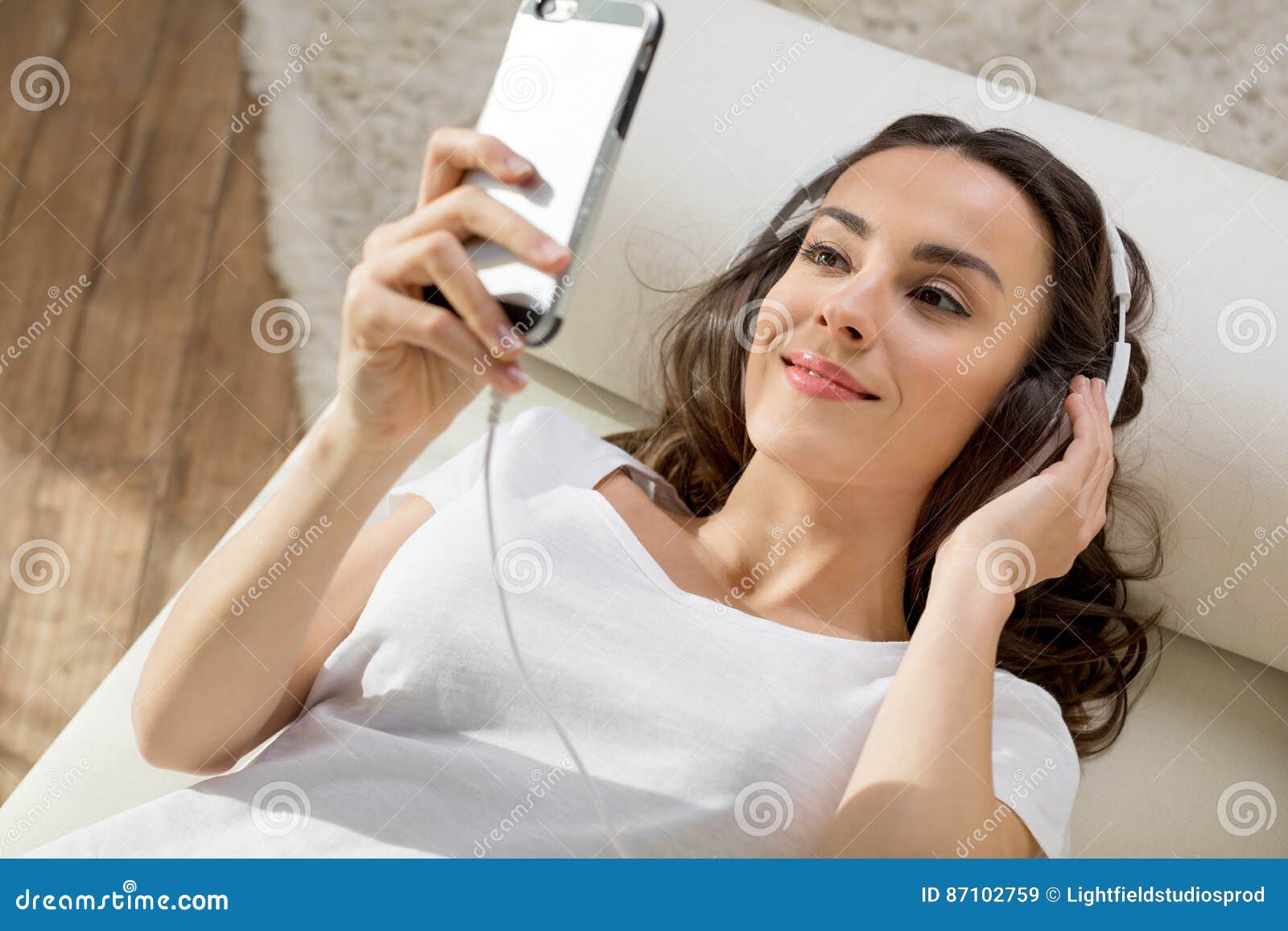 Young Woman In Headphones Using Smartphone While Lying On Sofa Stock 