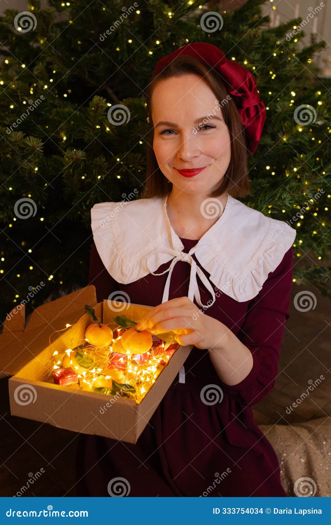 young woman holding gift box full of lights, mandarins and candies. christmas mood celebration. girl sitting on the