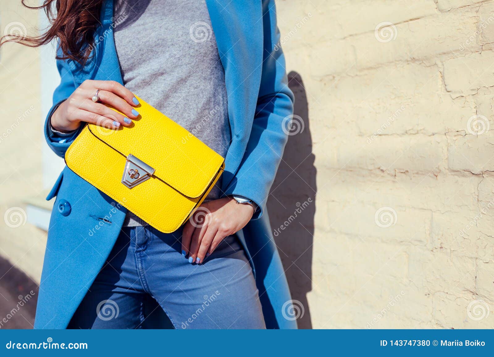 young woman holding stylish handbag and wearing trendy blue coat. spring female clothes and accessories. fashion