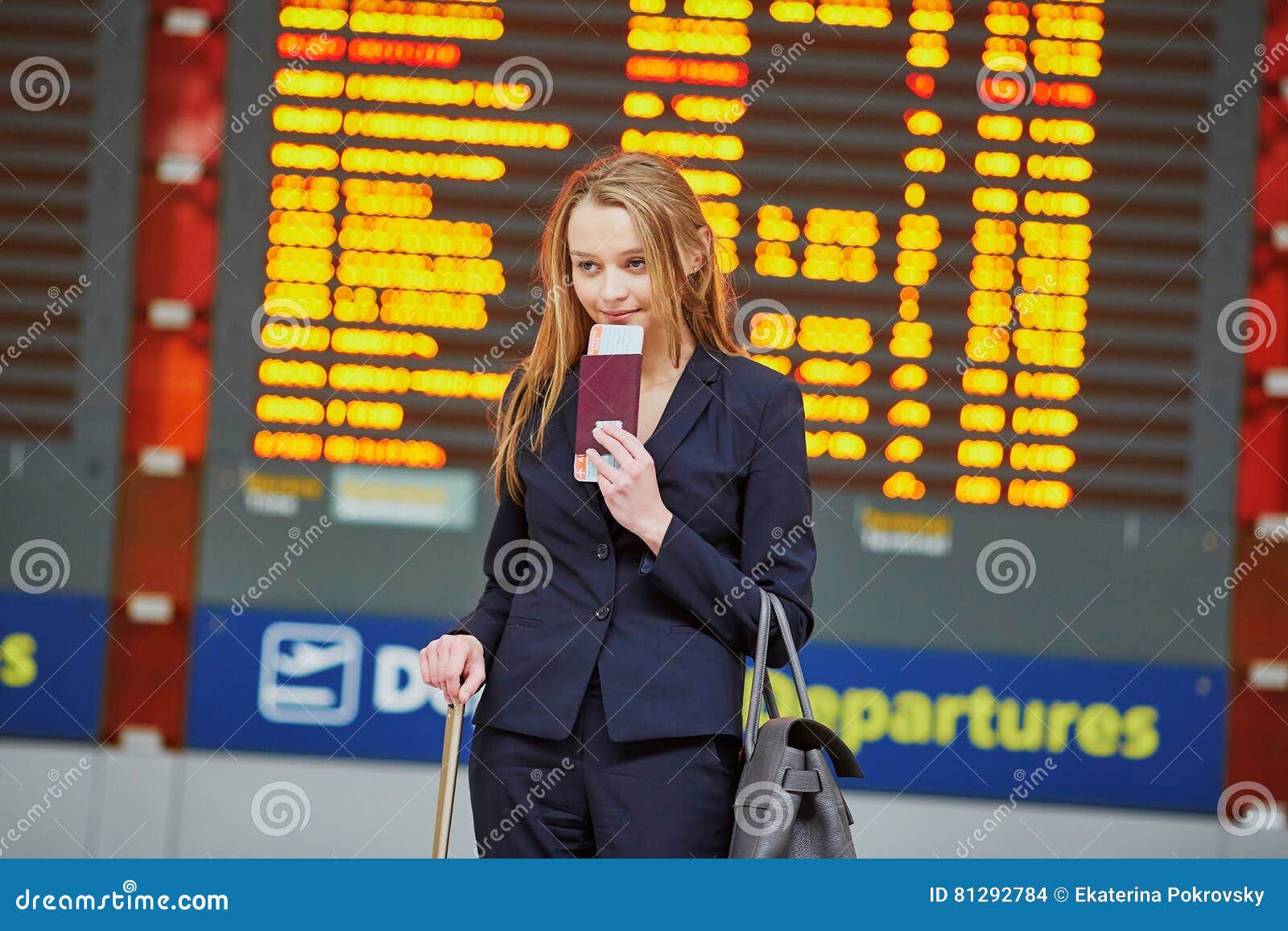Young woman in international airport looking at the flight information board, checking her flight. Young elegant business woman with hand luggage in international airport terminal, looking at information board, checking her flight. Cabin crew member with suitcase.