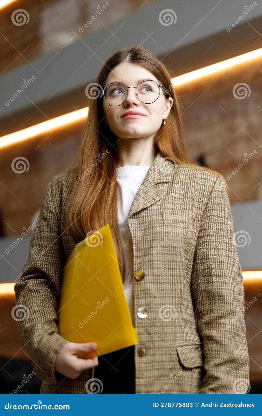 a young woman in a jacket with a yellow folder on the background of the office, purposefulness