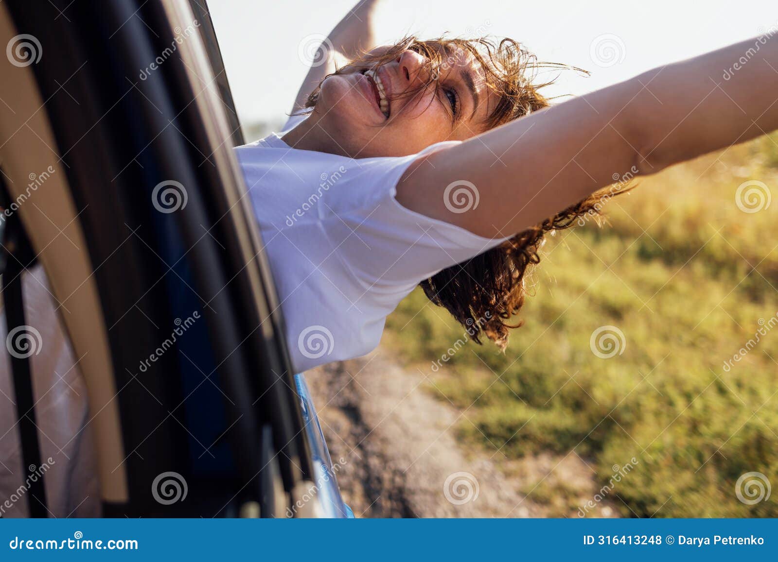 young woman leans out of car window and laughs. smiling girl travels and has fun on road
