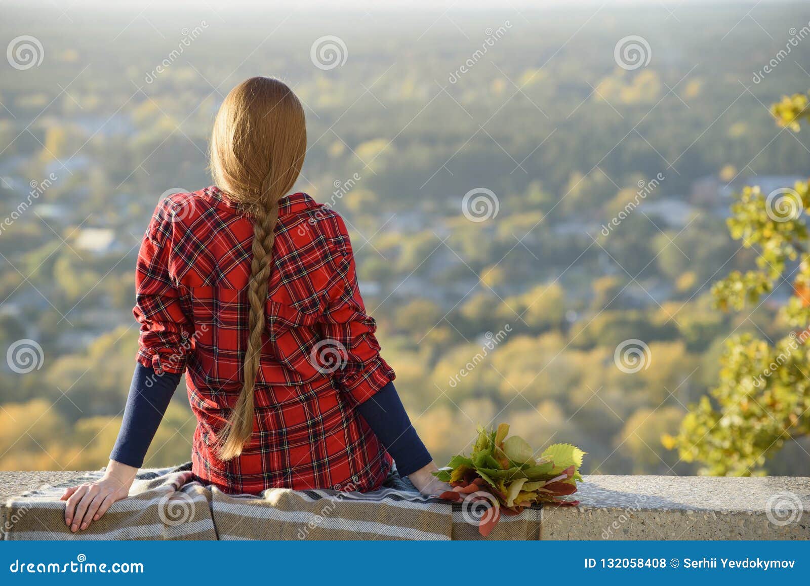 young woman with long hair sits on a hill overlooking the city