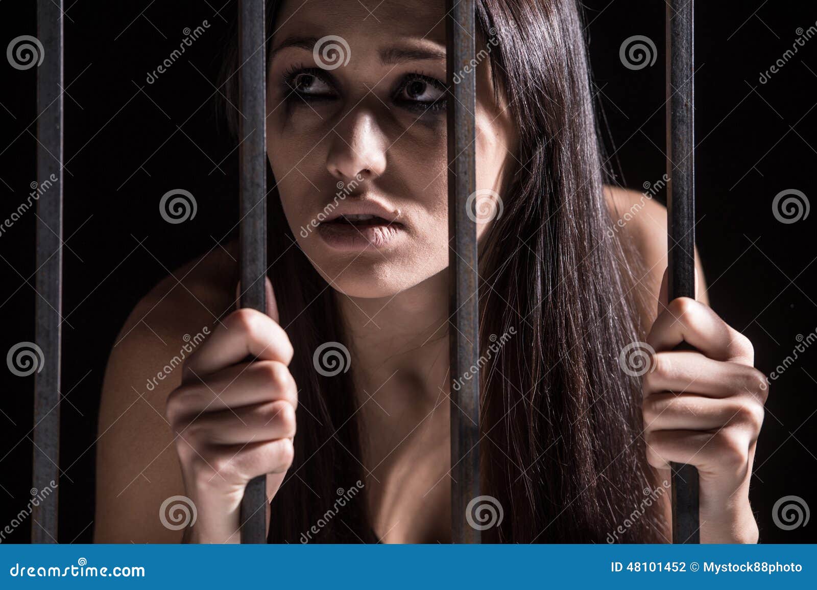 young woman looking from behind bars.