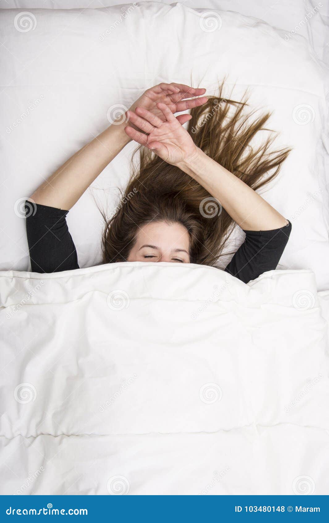 young woman is lying in her bed with closed eyes, smiling under her blanket after a restful sleep.