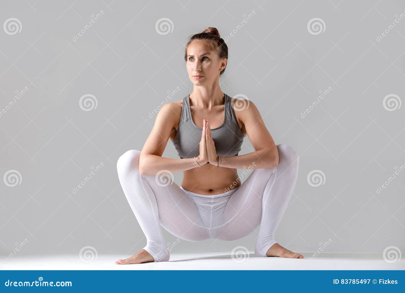 young woman malasana pose grey studio background attractive practicing yoga sitting garland exercise working out wearing 83785497