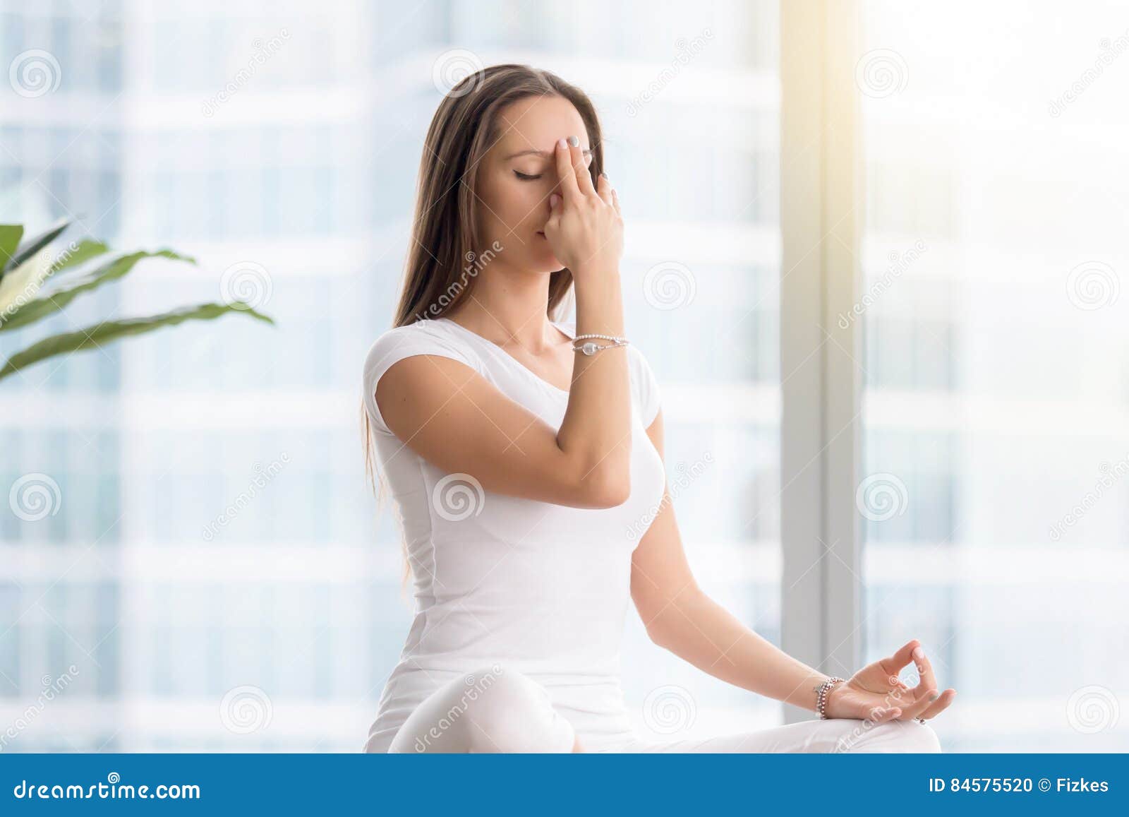 young woman in nadi shodhana pranayama against floor window