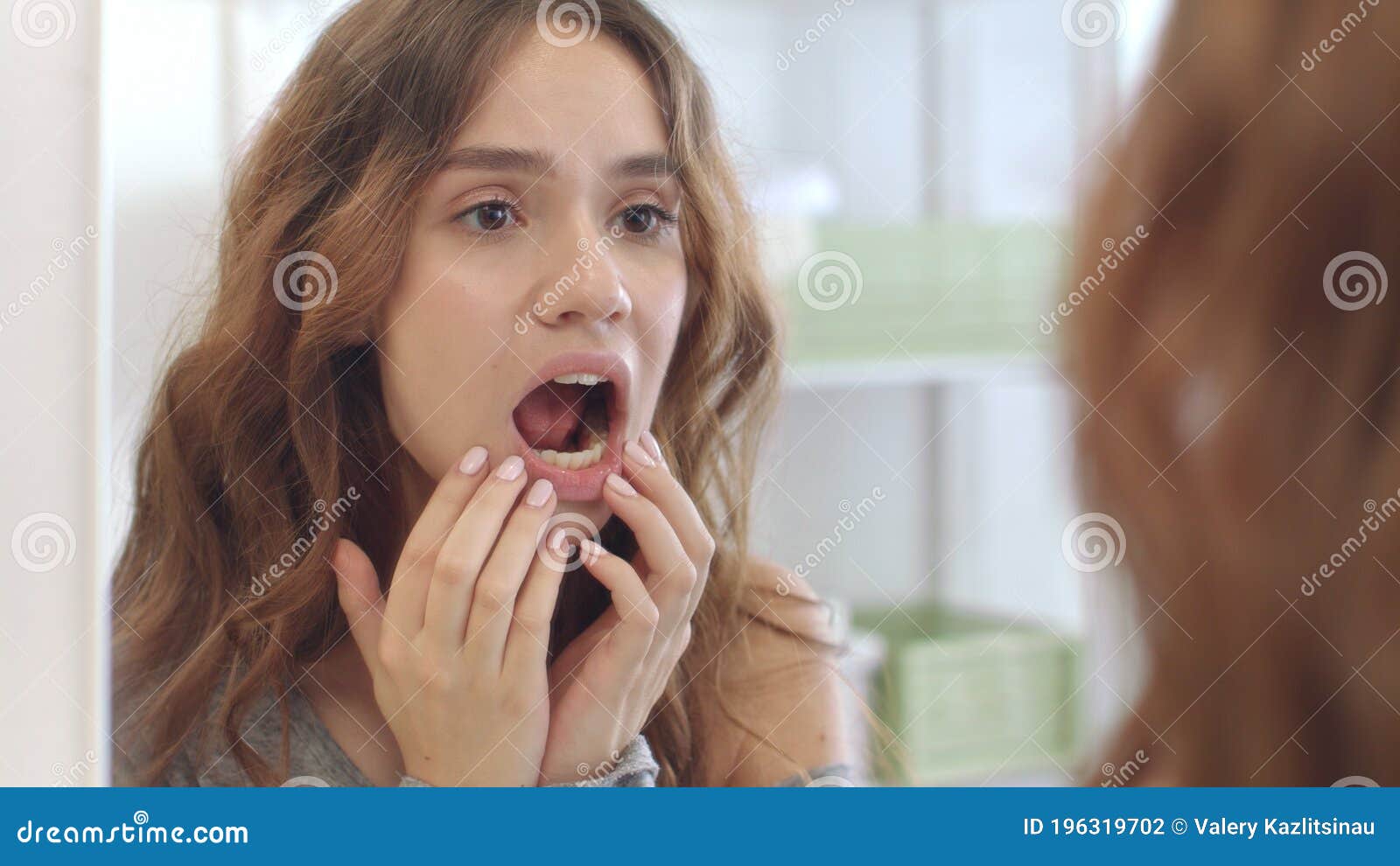 young woman with opened mouth checking teeth in mirror in home bath room