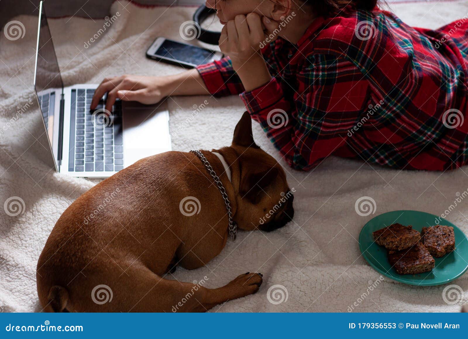young woman in pijama using laptop with french bulldog next to her