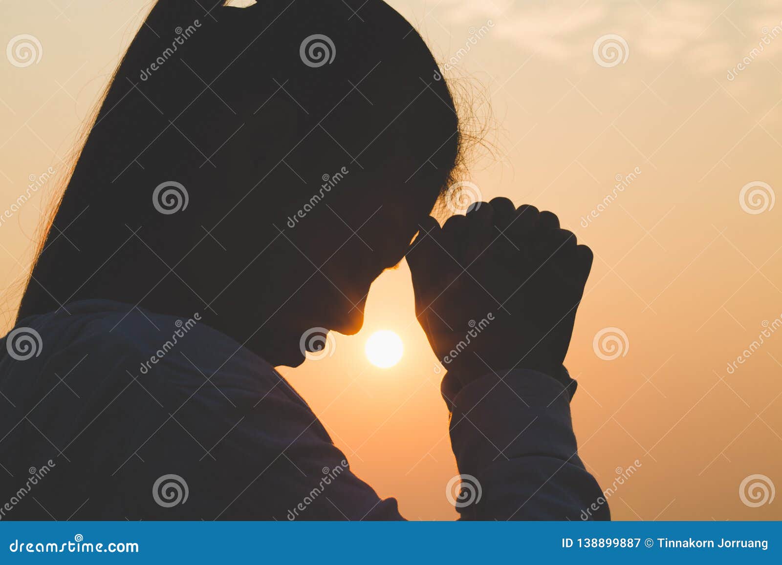young woman praying in the morning, hands folded in prayer concept for faith, spirituality and religion
