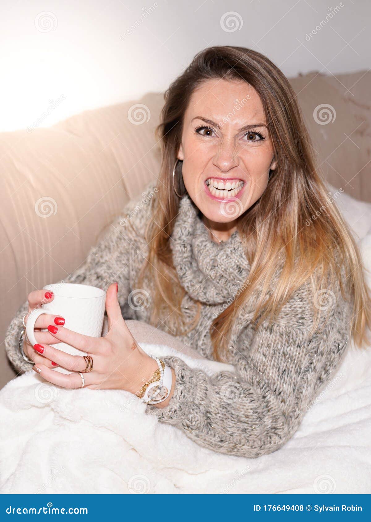 young woman pretends to growl sitting on home couch in house drinking tea hot drink coffee in winter day
