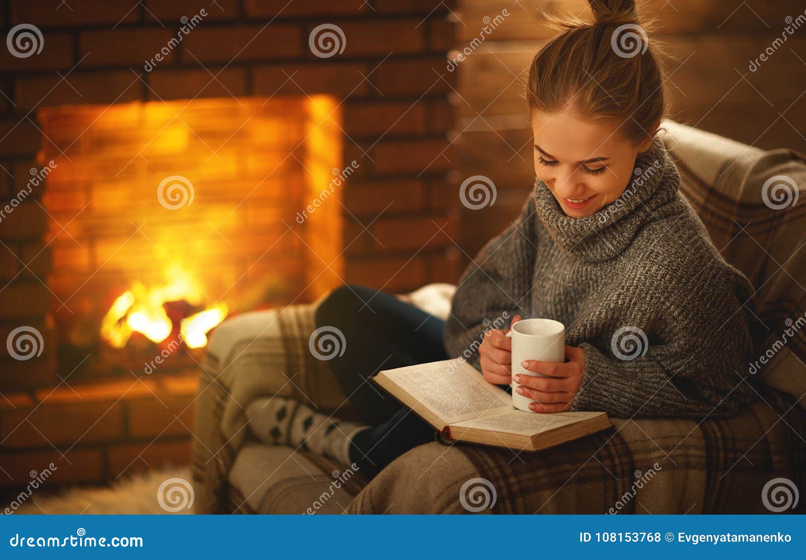 young woman reading a book by the fireplace on a winter evenin