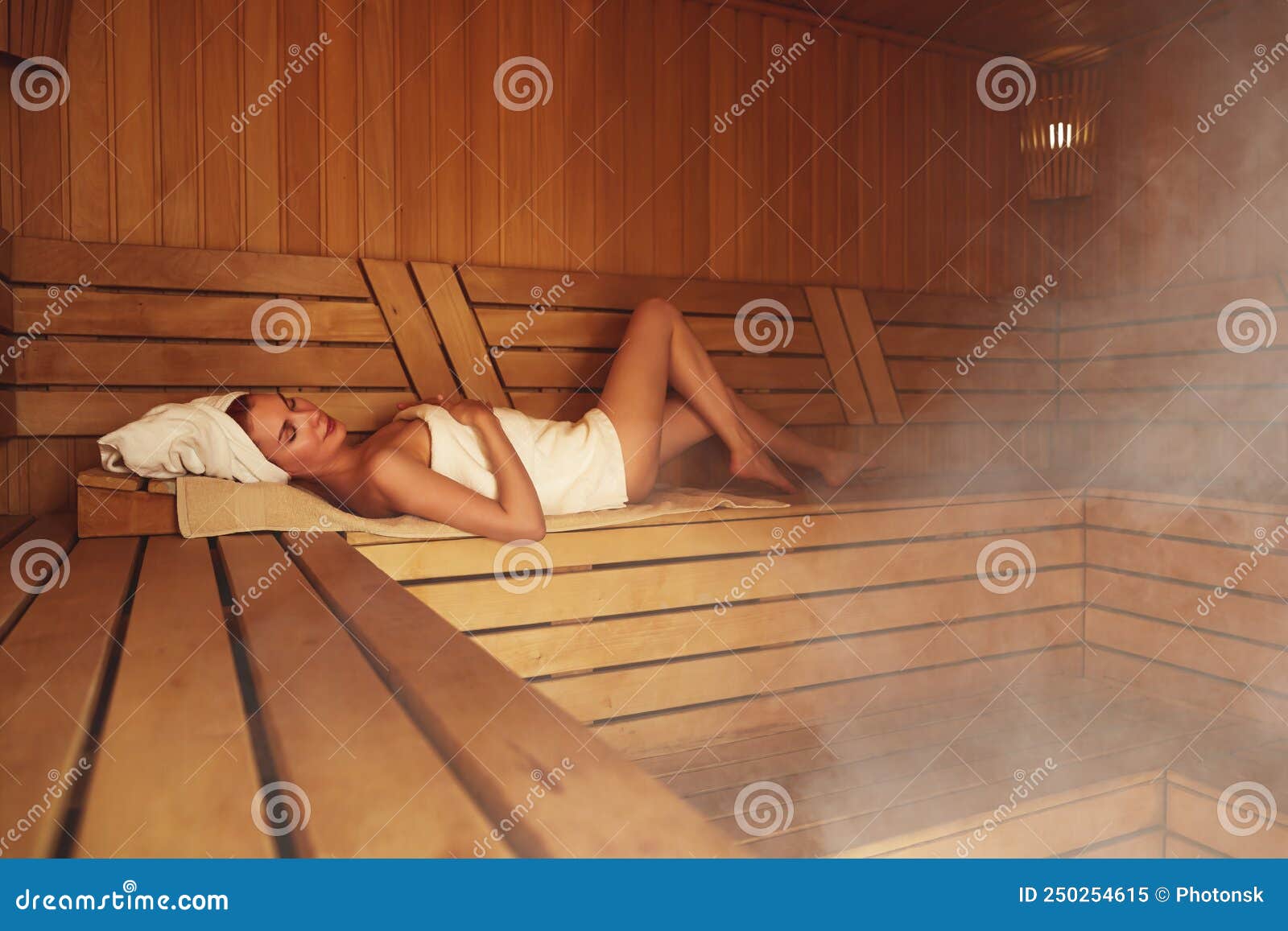 Young Woman Relaxing in a Sauna Dressed in a Towel. Interior of