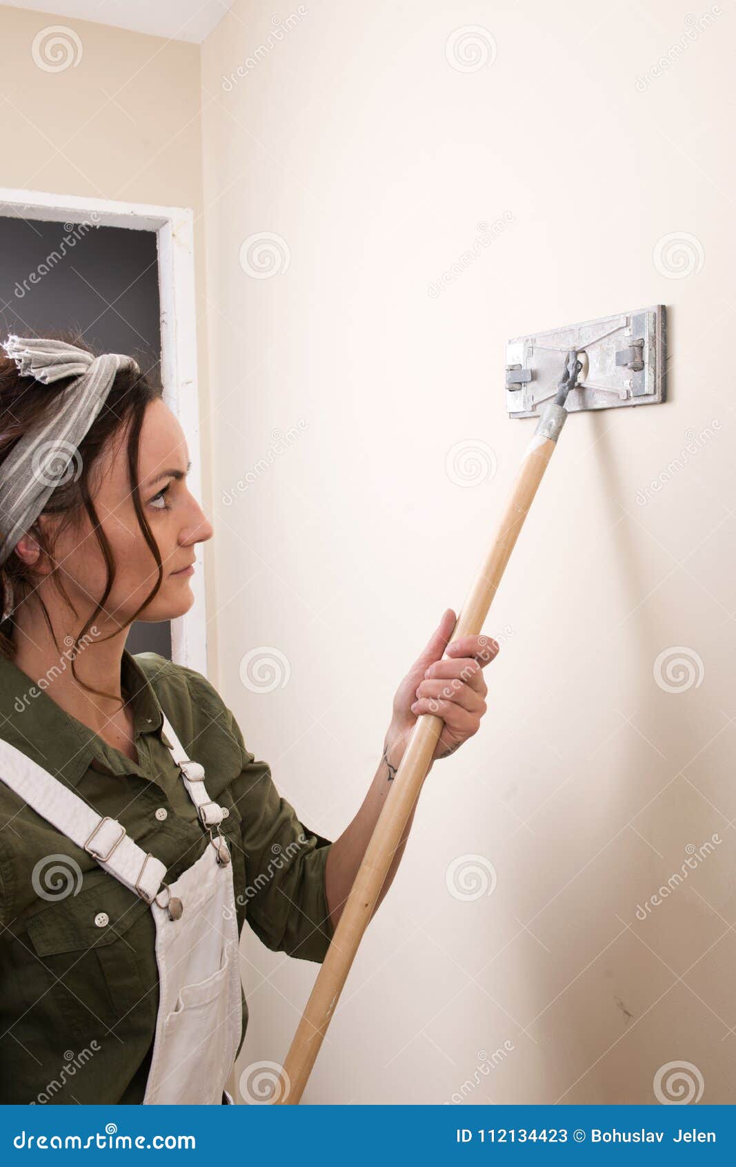 Young Woman Is Sanding Wall With Pole Sander Before Painting Stock