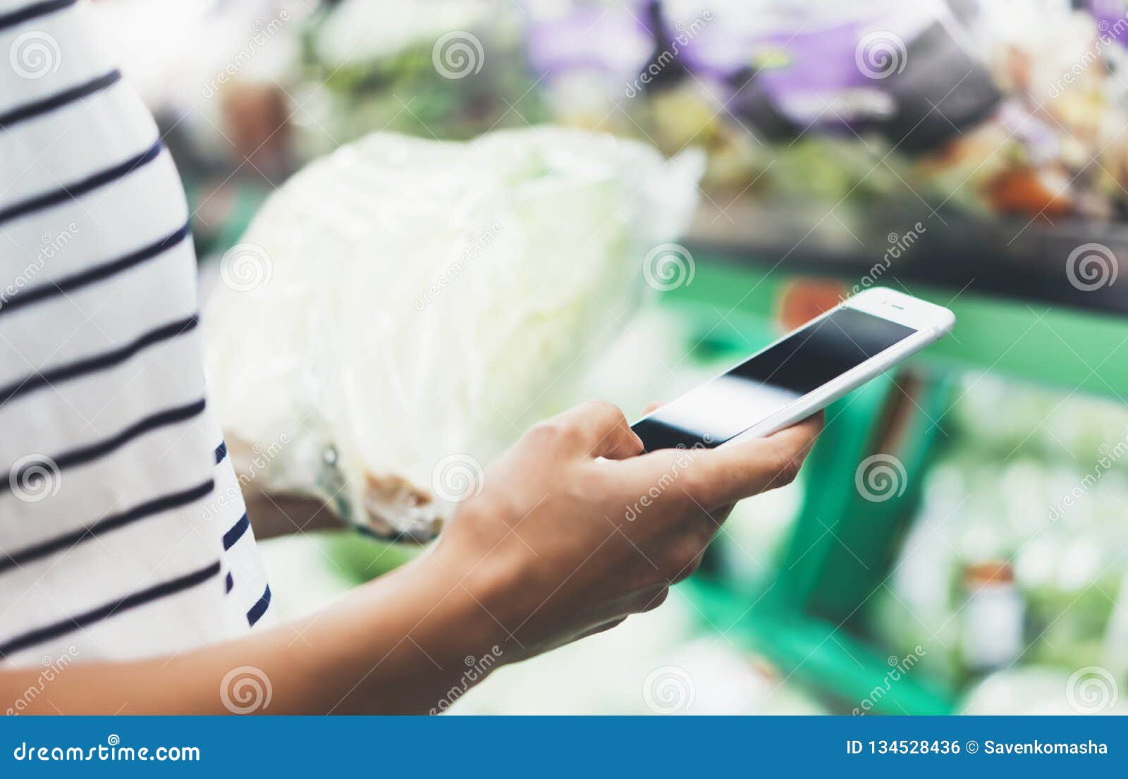 young woman shopping healthy food in supermarket blur background. female hands buy products cabagge using smartphone in store