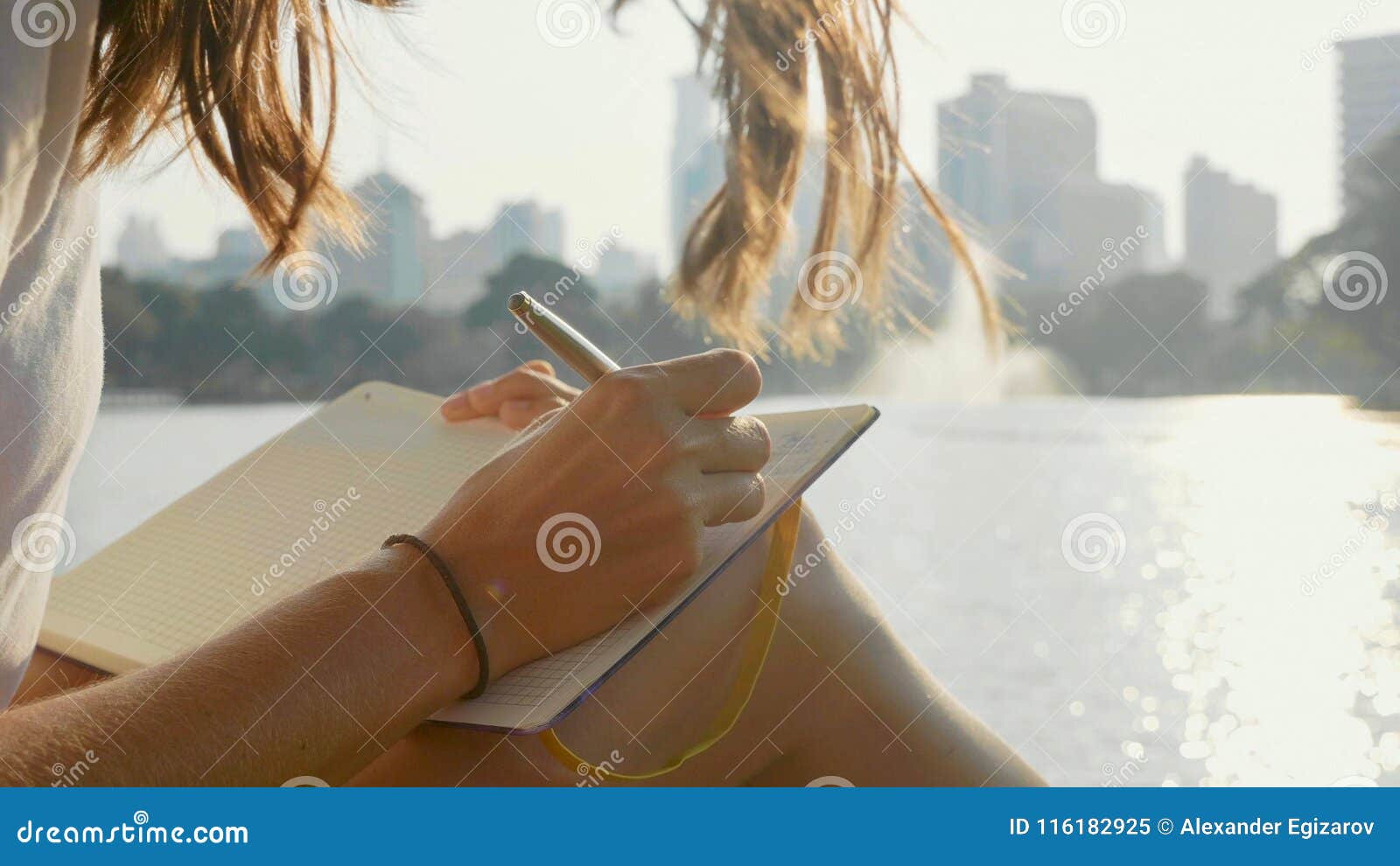 young woman sitting on the bench in park and writing in diary, close-up