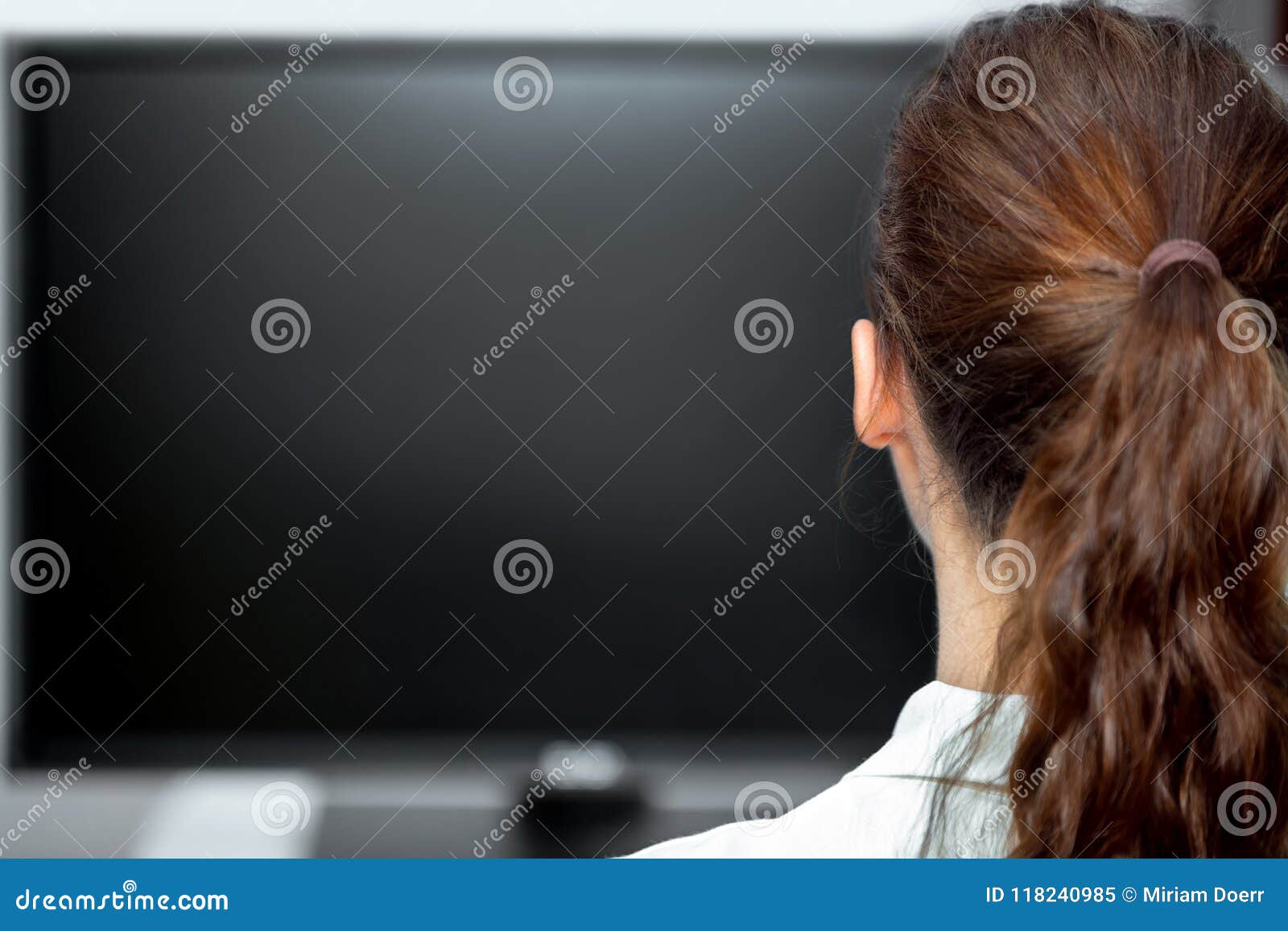 young woman sitting in front of a black monitor or tv, backview