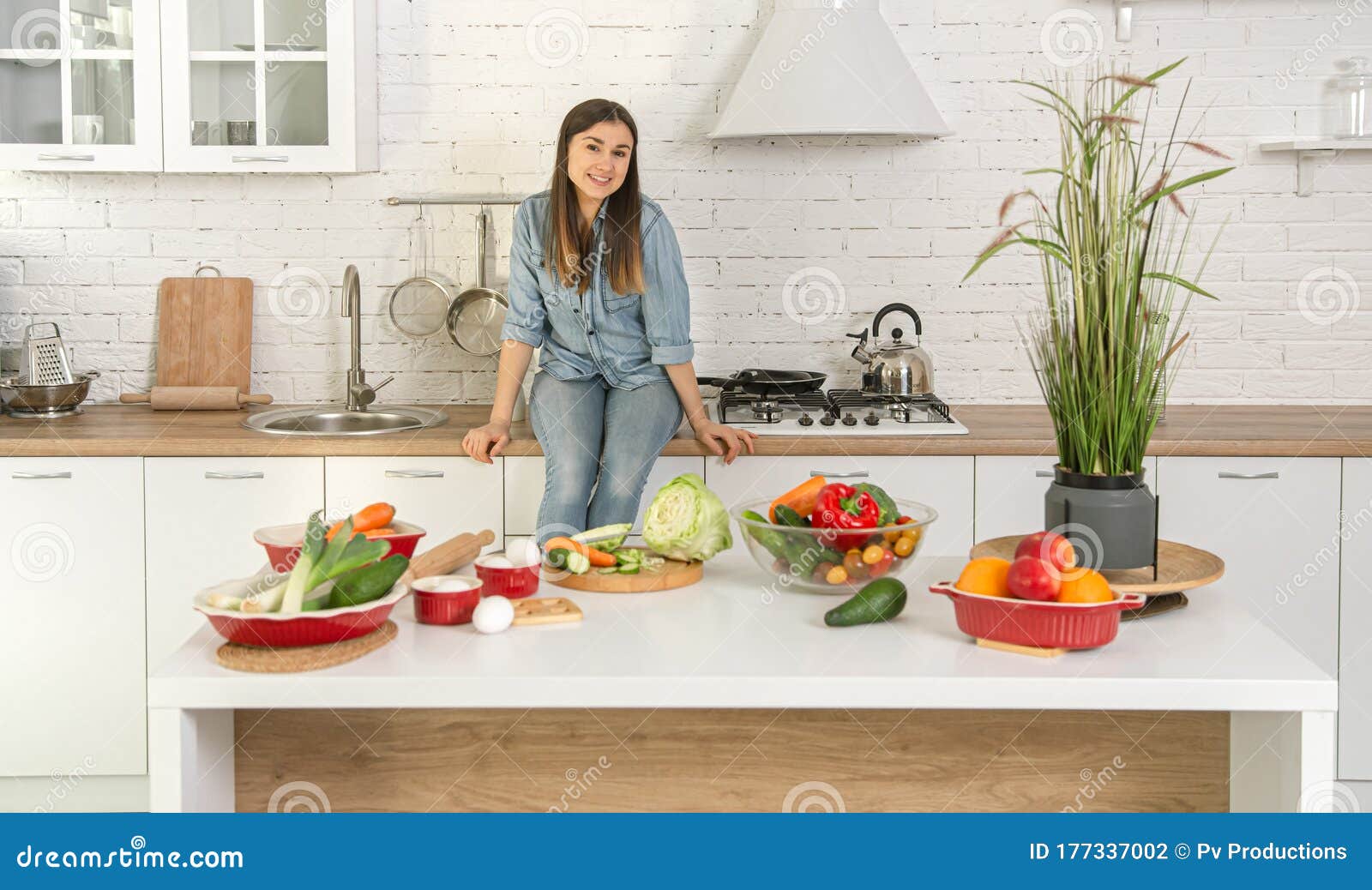 A Young Woman Is Sitting On The Kitchen Table With Vegetables And