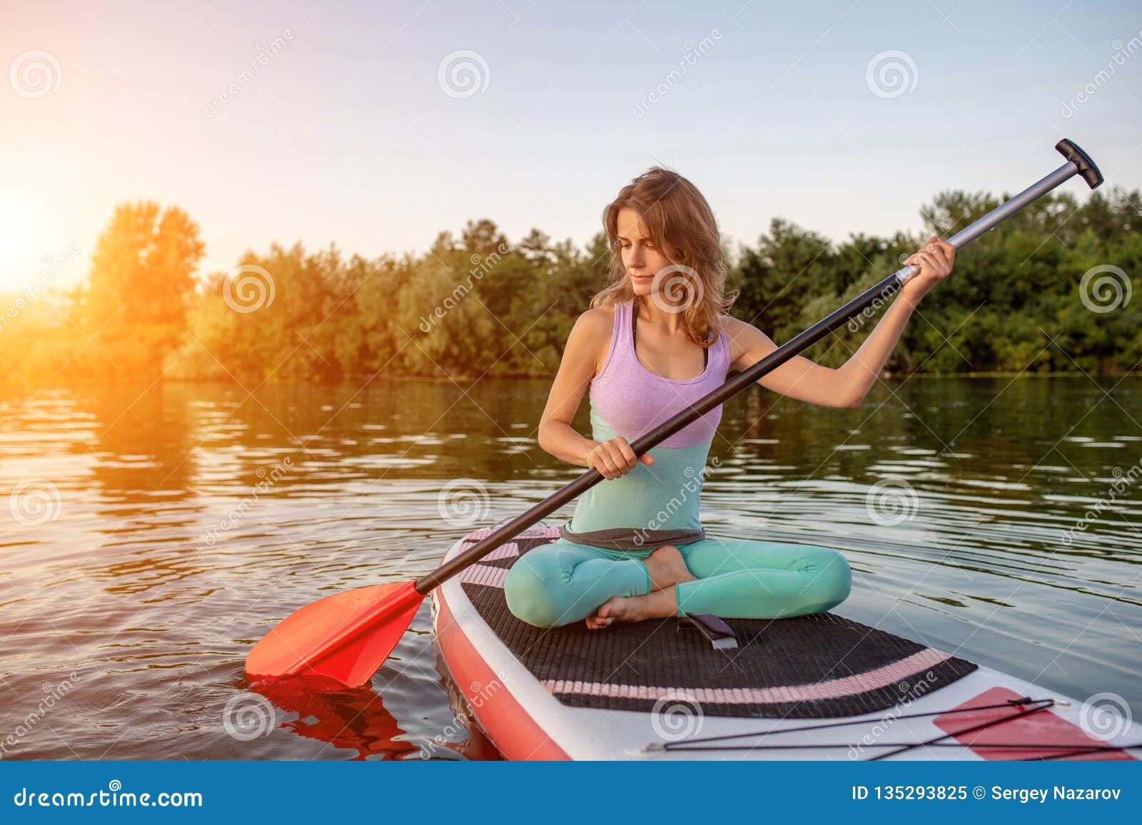 Young Woman Sitting on Paddle Board, Practicing Yoga Pose. Doing Yoga ...