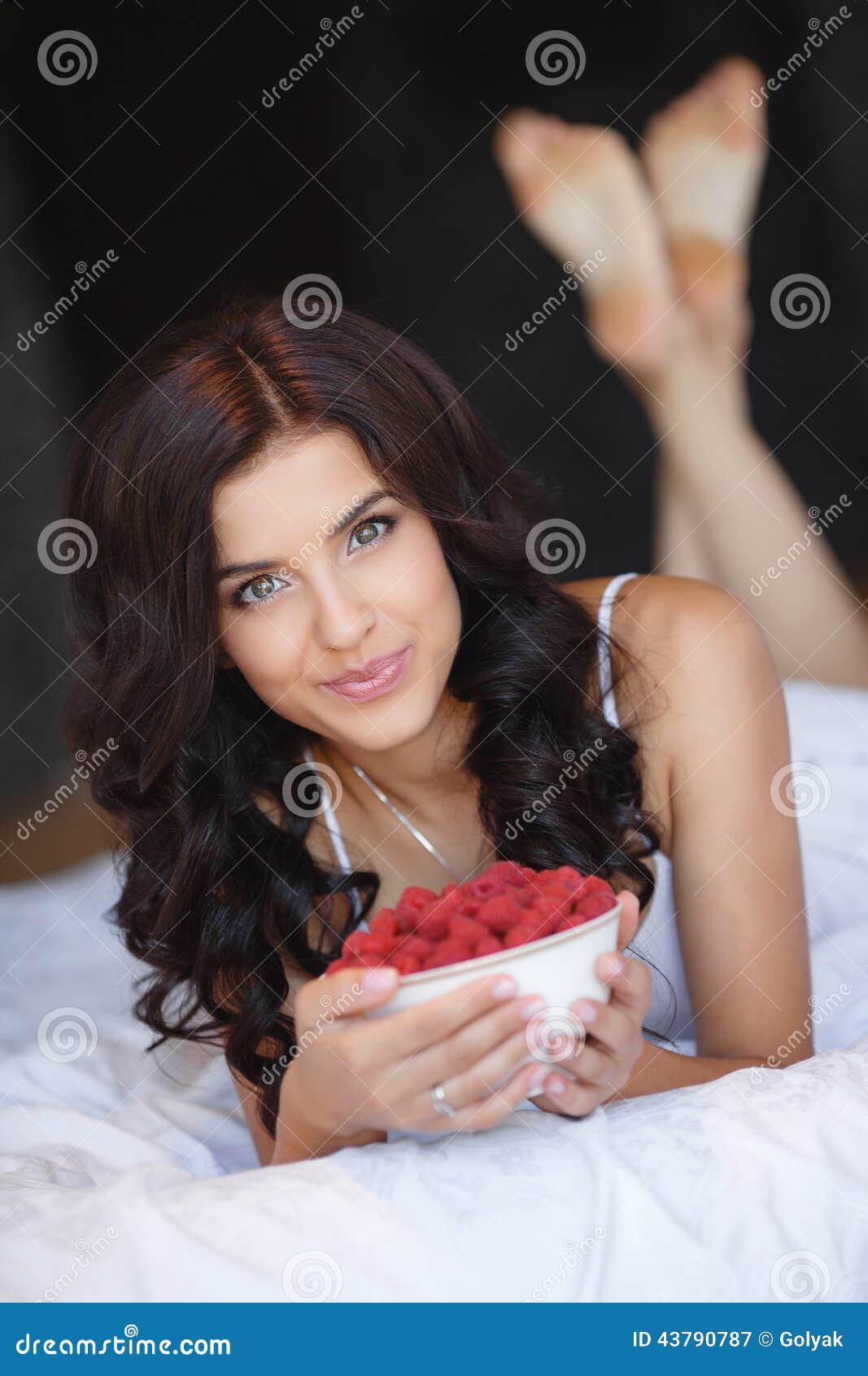 Young woman smiling eating fruit salad raspberry. Beautiful, happy, young woman with perfect teeth, smiling &amp; eating healthy fruit salad of strawberries, raspberries &amp; blueberries in a bowl