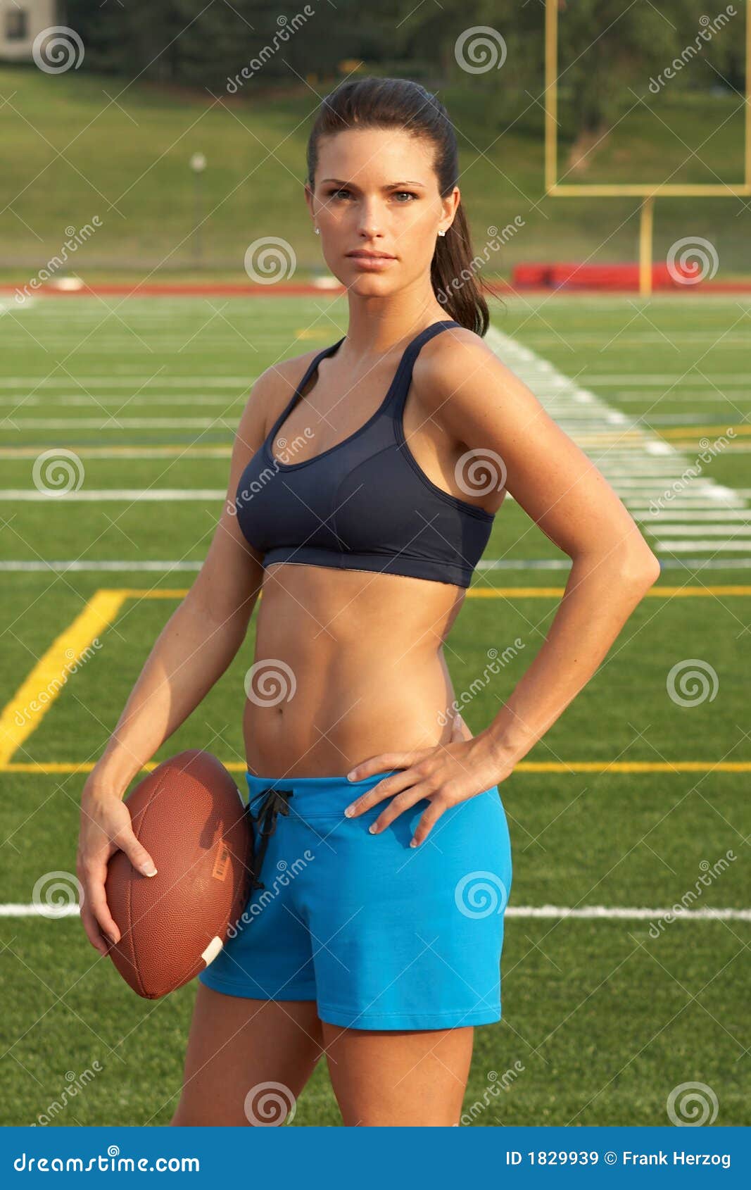 Young Woman in Sports Bra Holding Football with Hand on Hip Stock