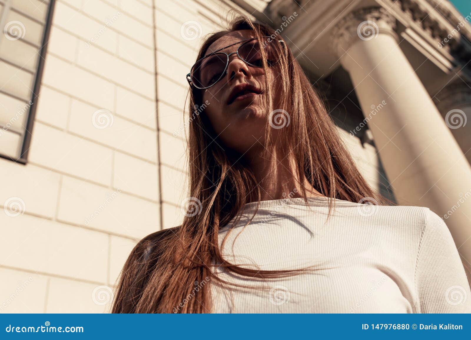 young woman standing on the wall of the bilding backgroundand looking at camera