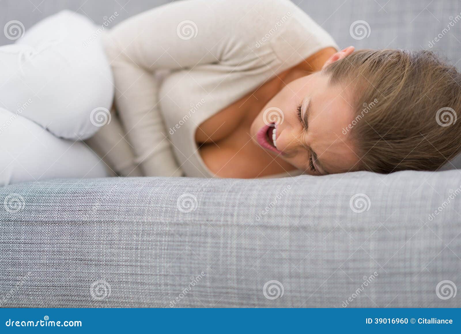 Young woman with stomach ache laying on sofa in living room