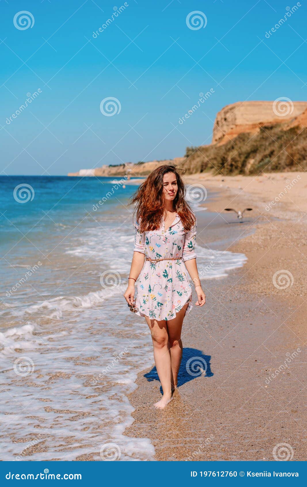 young woman in sunglasses and dress on the beach in front of the sea