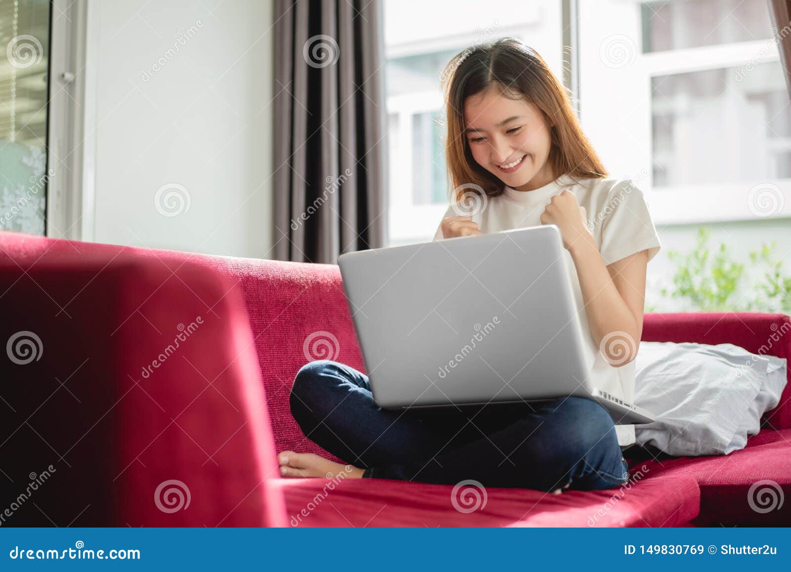 young woman surfing the internet by laptop on red sofa and glad in successful trading in her house. selling and online shopping