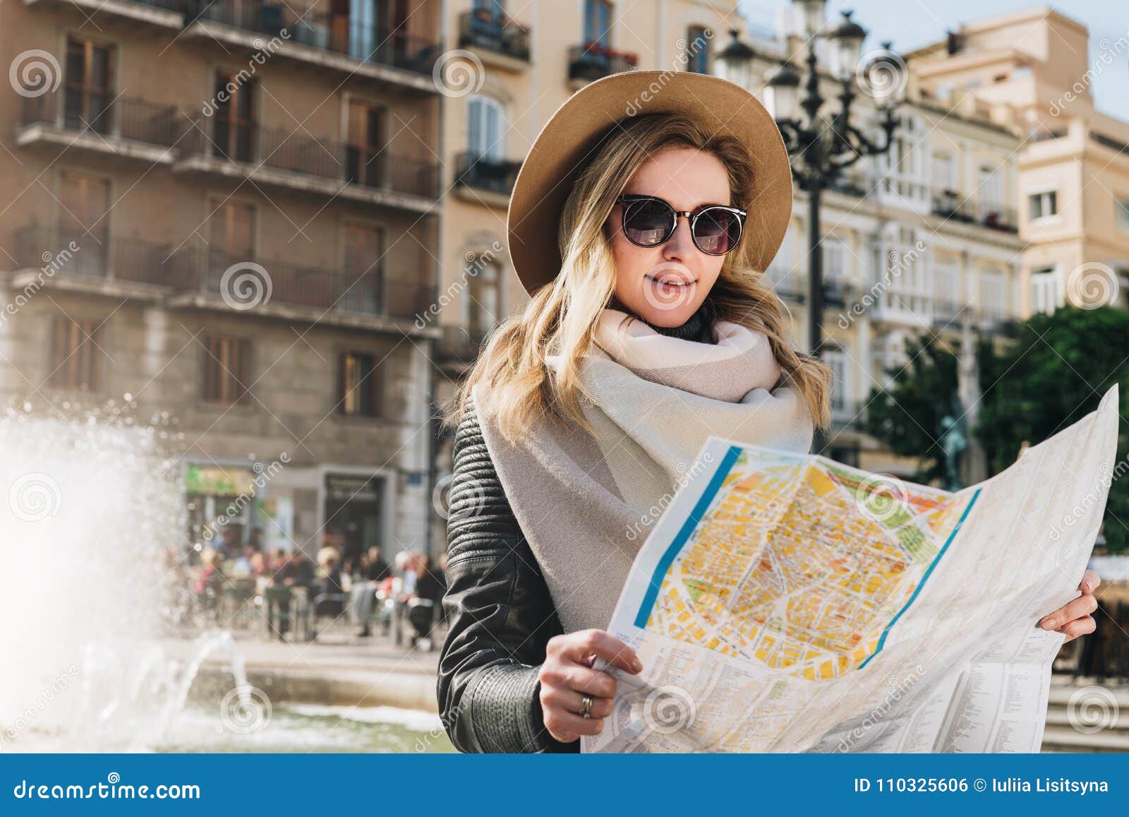 young woman tourist stands on street of ancient european city and holds map. in background is beautiful building.