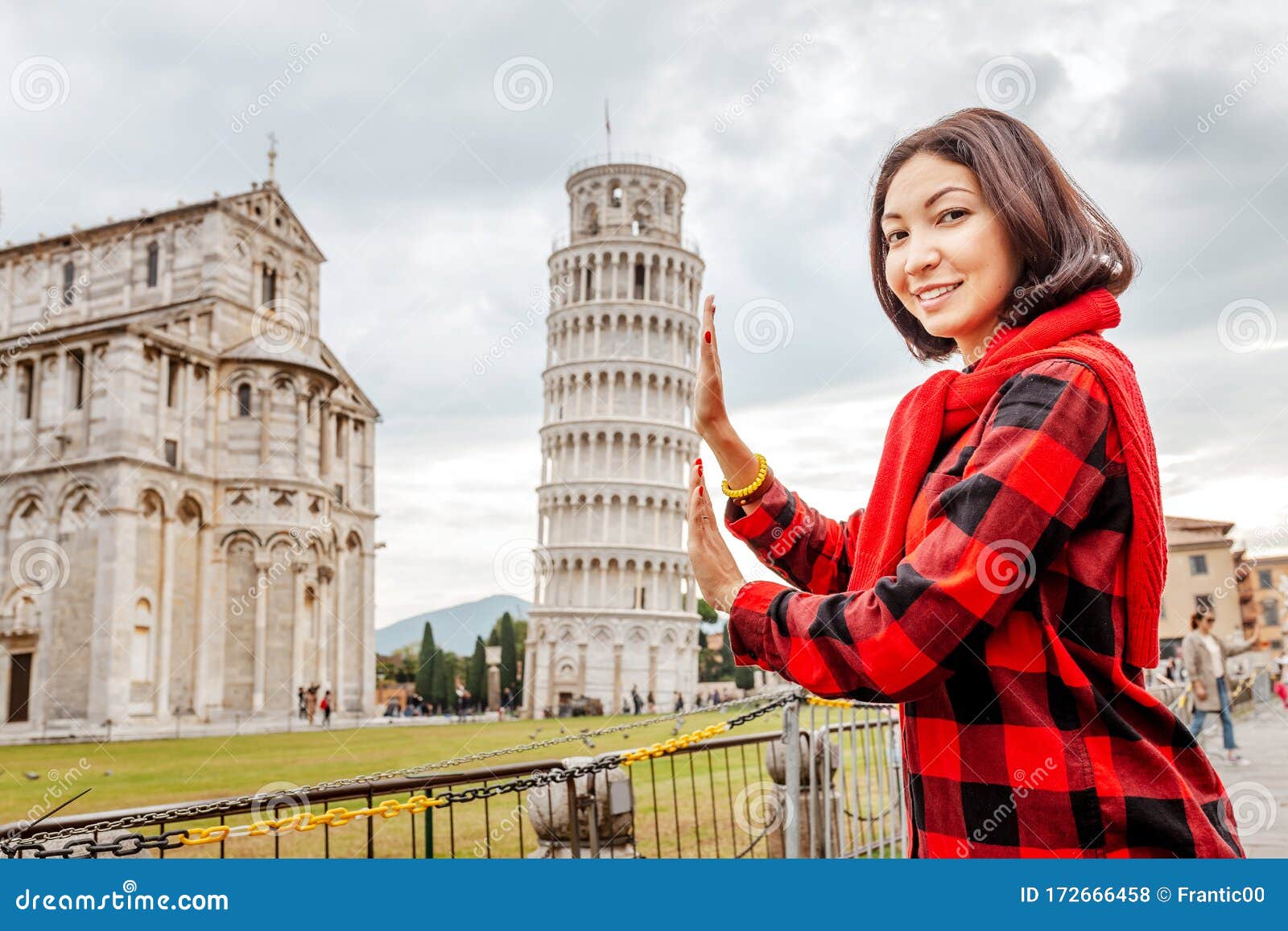 woman traveler making funny poses in front of the famous leaning tower in pisa, italy. happy travel photos in italy concept