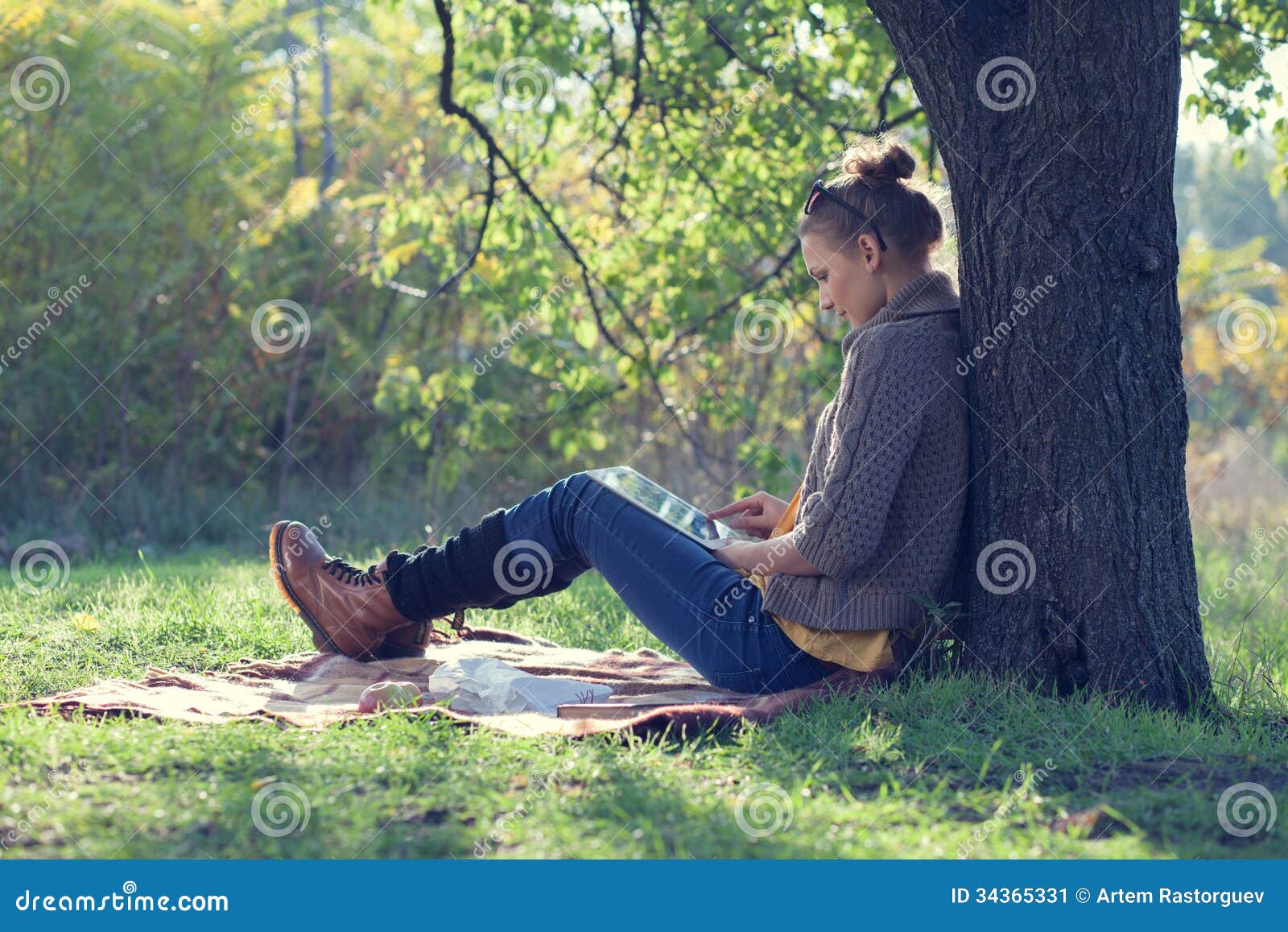 Hipster style young woman using tablet pc during a rest under the tree