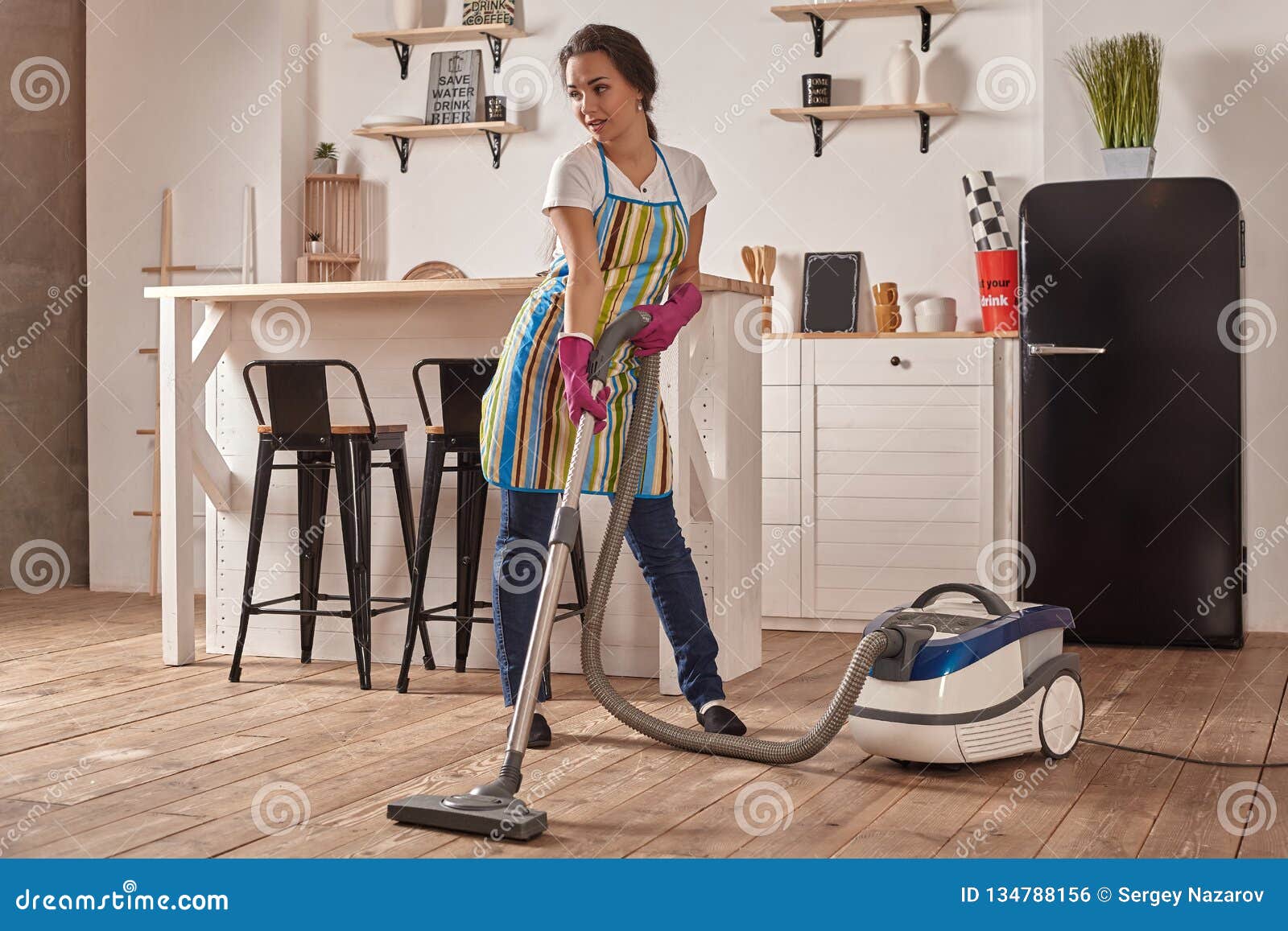 Young Woman Using Vacuum Cleaner In Home Kitchen Floor Doin