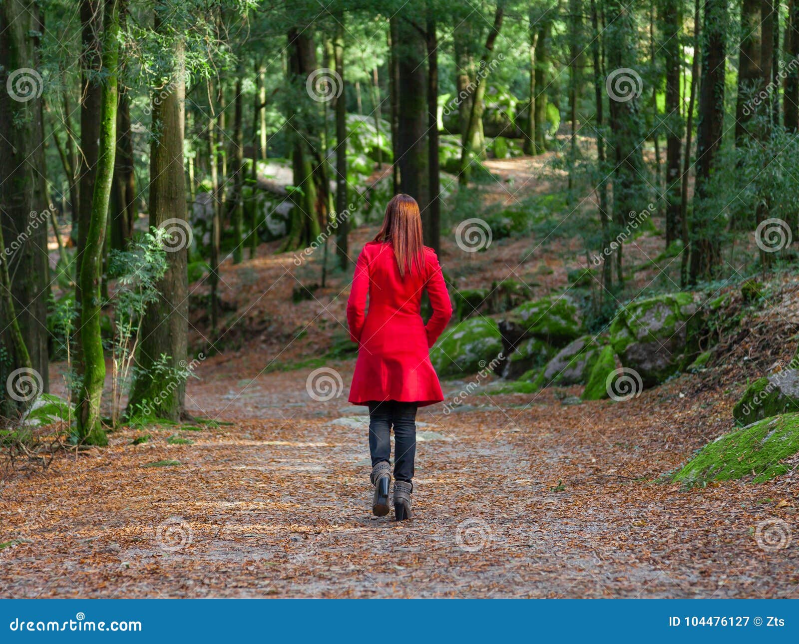 young woman walking away alone on forest path wearing red long coat