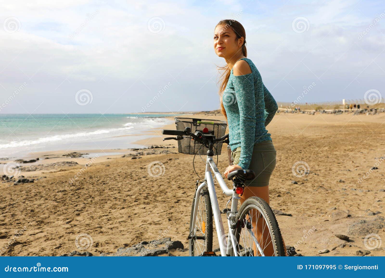 young woman walking with bicycle on beach enjoying view of atlan