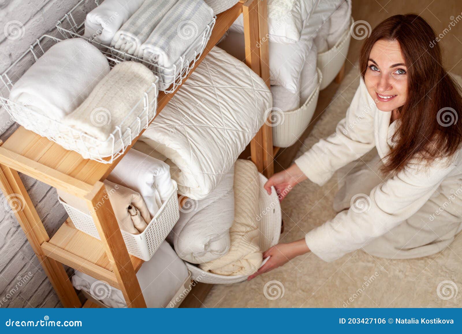 young woman in warm robe is organizing linen closet with neatly folded towels, sheets and blankets.