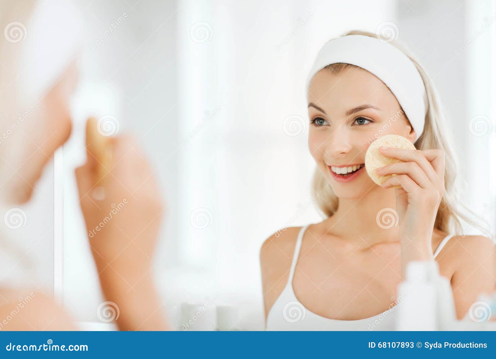 young woman washing face with sponge at bathroom