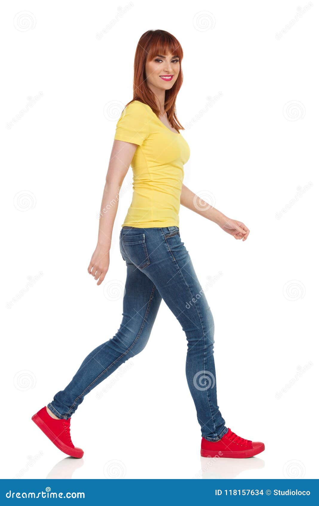 Happy casual young woman in yellow shirt, jeans and red sneakers