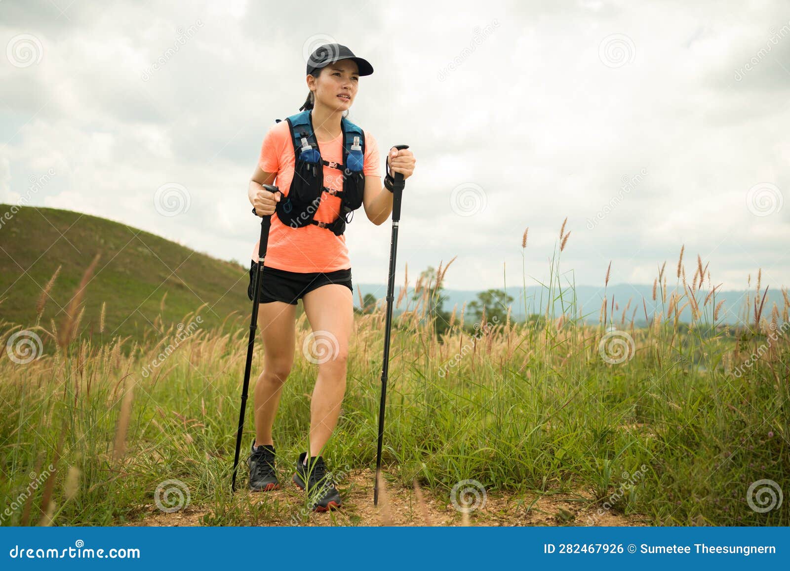 young women active trail running across a meadow on a grassy trail high in the mountains in the afternoon with trekking pole