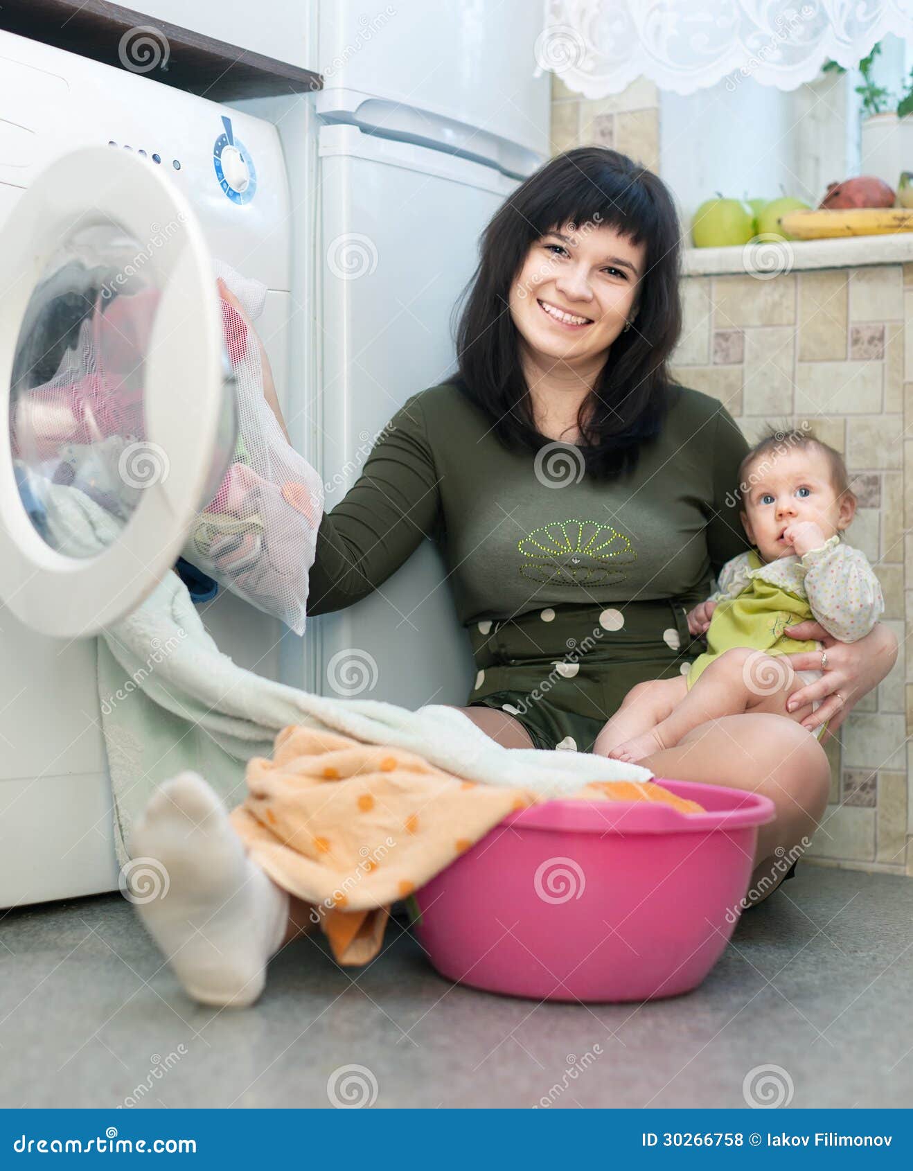 Woman With Baby Putting Clothes In To Washing Machine ...