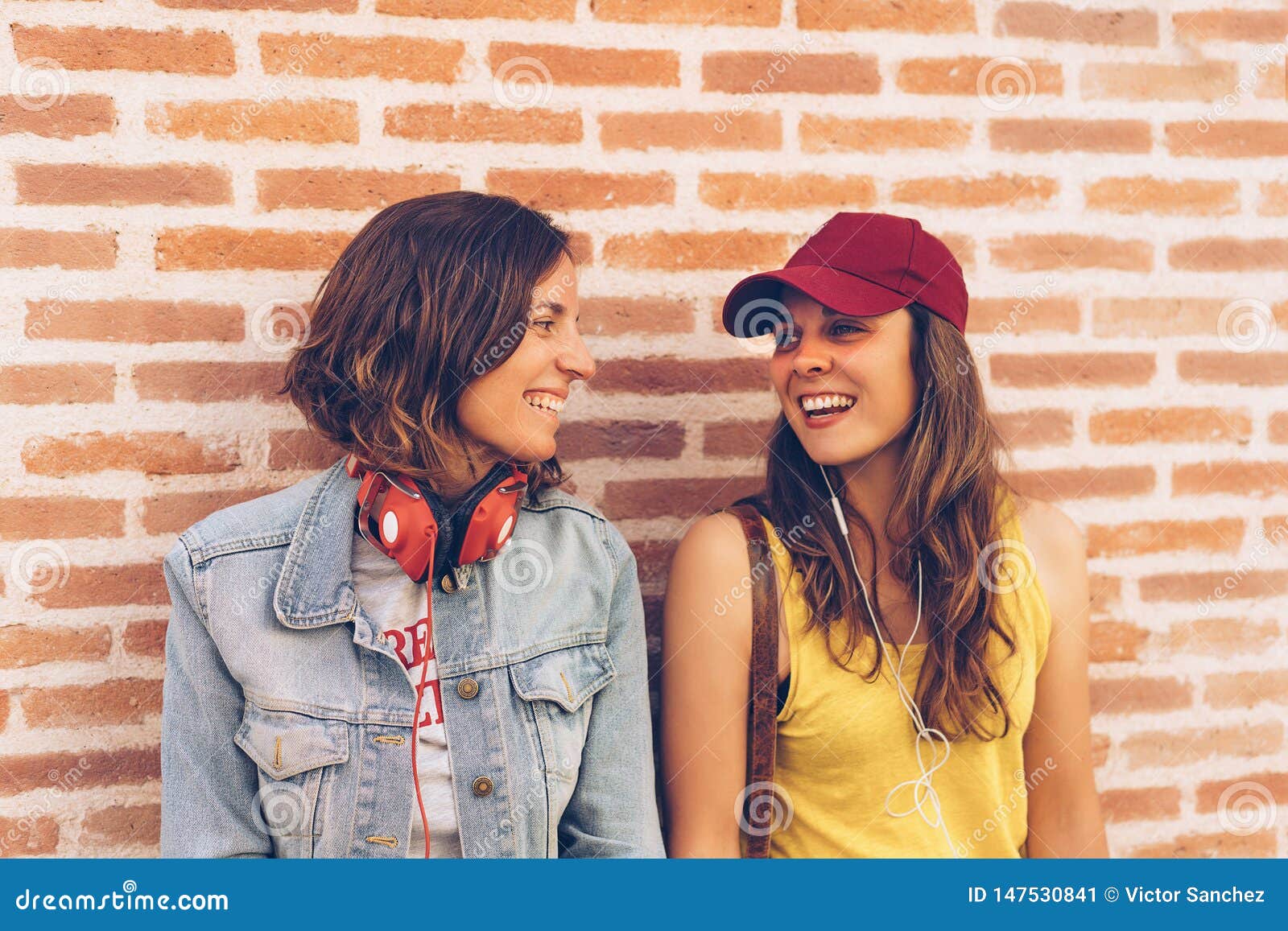Young Women Couple Looking and Smiling Each Other in a Brick Wall Background image